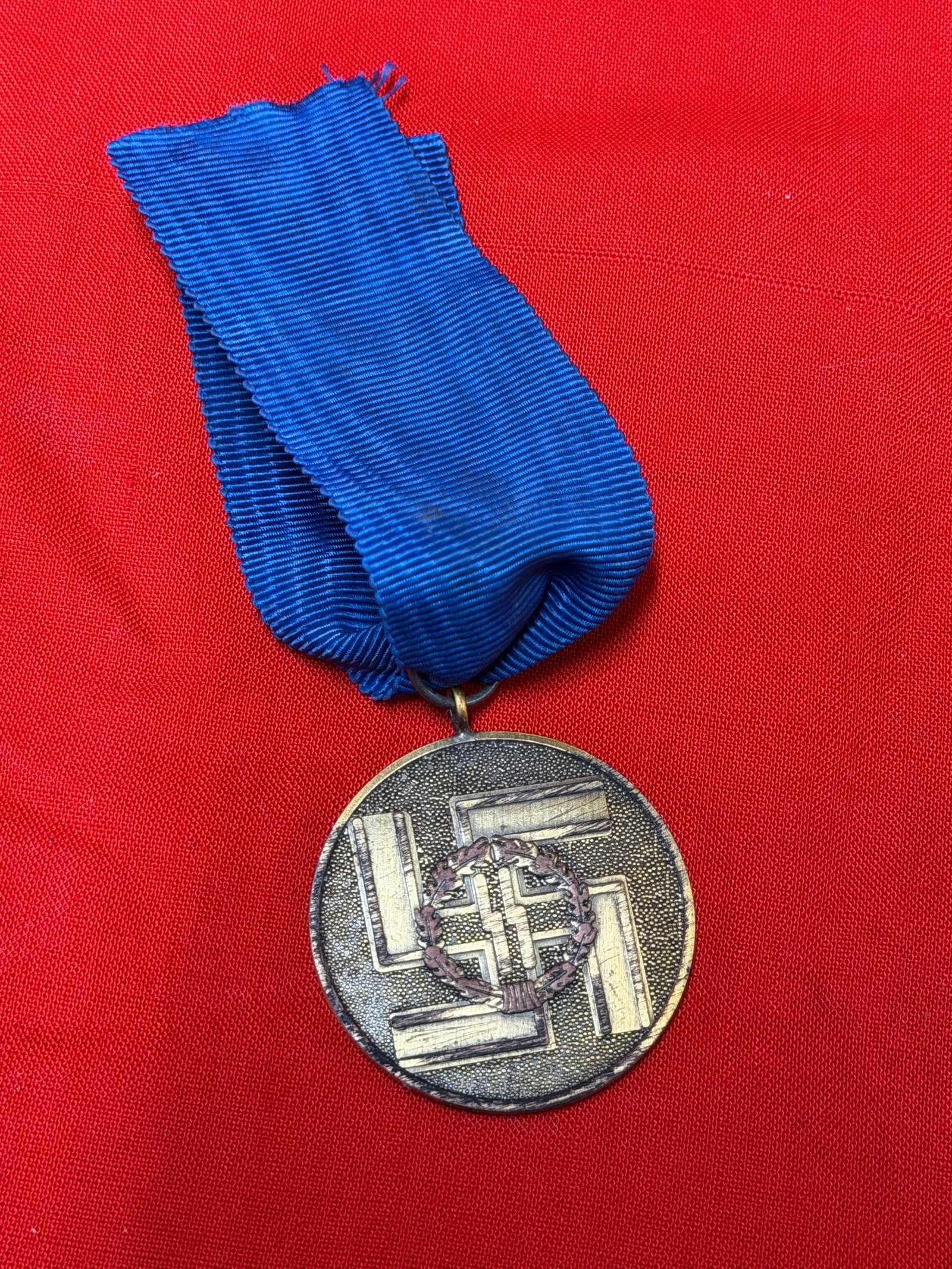 An impressive militaria collectible, ideal for advanced WWII German artifact collectors, historical: WWII German Waffen-SS long service medal featuring the classic blue ribbon and detailed circular medal design. The obverse displays the SS runes within a wreath and swastika motif, while the reverse i