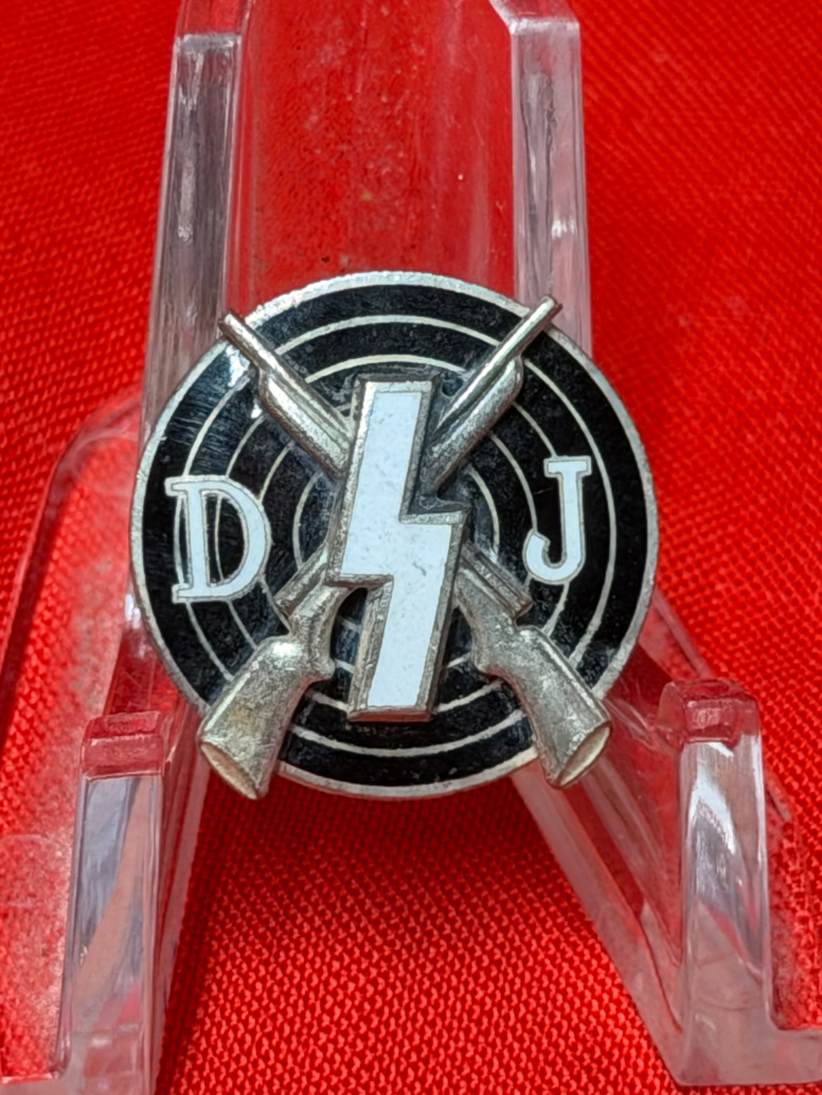 WW2 German DJ Shooting Sports Rifle Target Pin Badge M1/23: This vintage German shooting sports style pin features crossed rifles over a black target design with the letters “D” and “J” alongside a central lightning bolt emblem. In our opinion,
