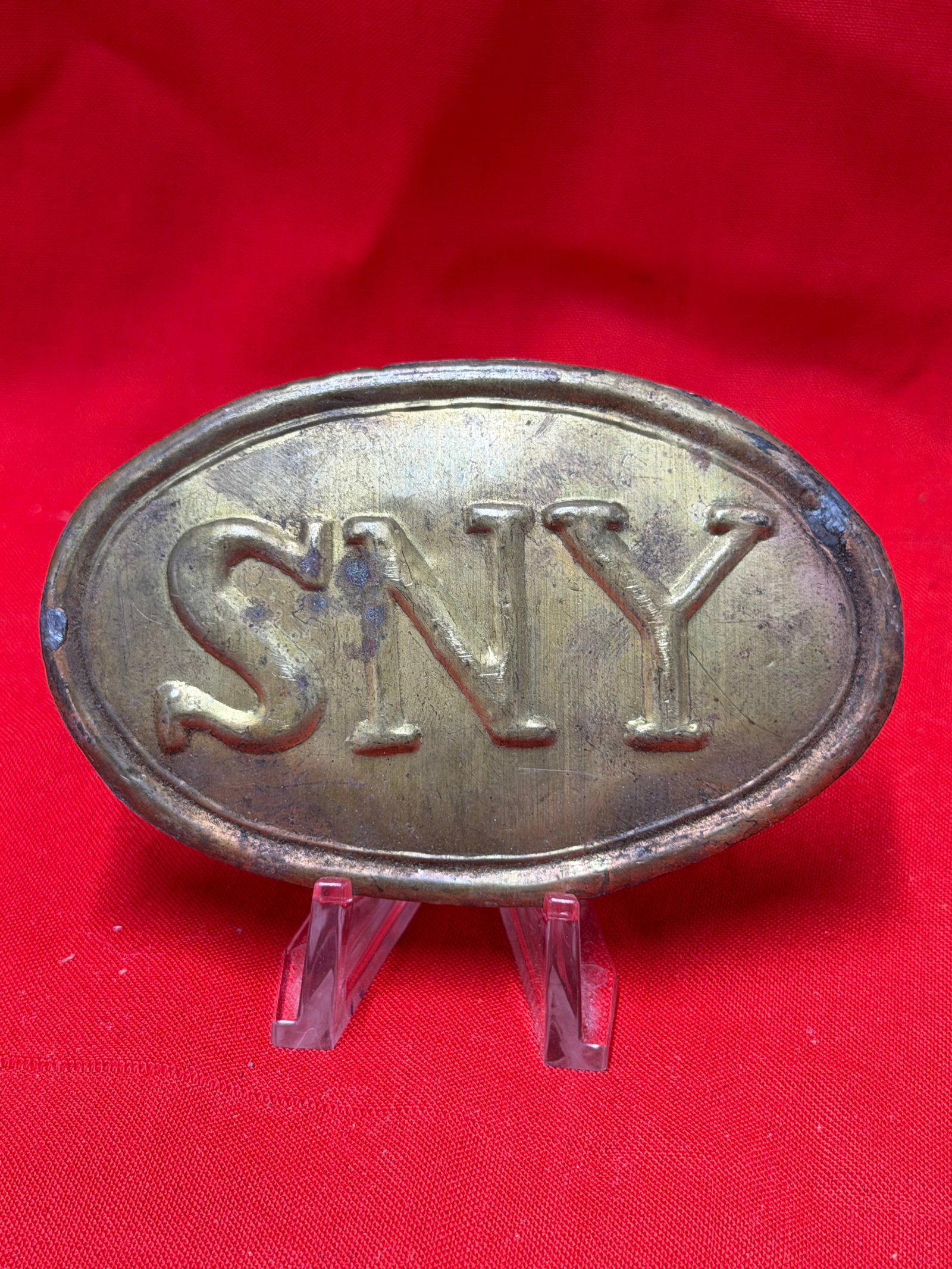 SNY Civil War Union Belt Plate Brass Buckle Display Piece: Oval brass tone belt plate featuring raised “SNY” lettering associated with New York military insignia. In our opinion this piece appears to be styled after Civil War era Union belt plates and