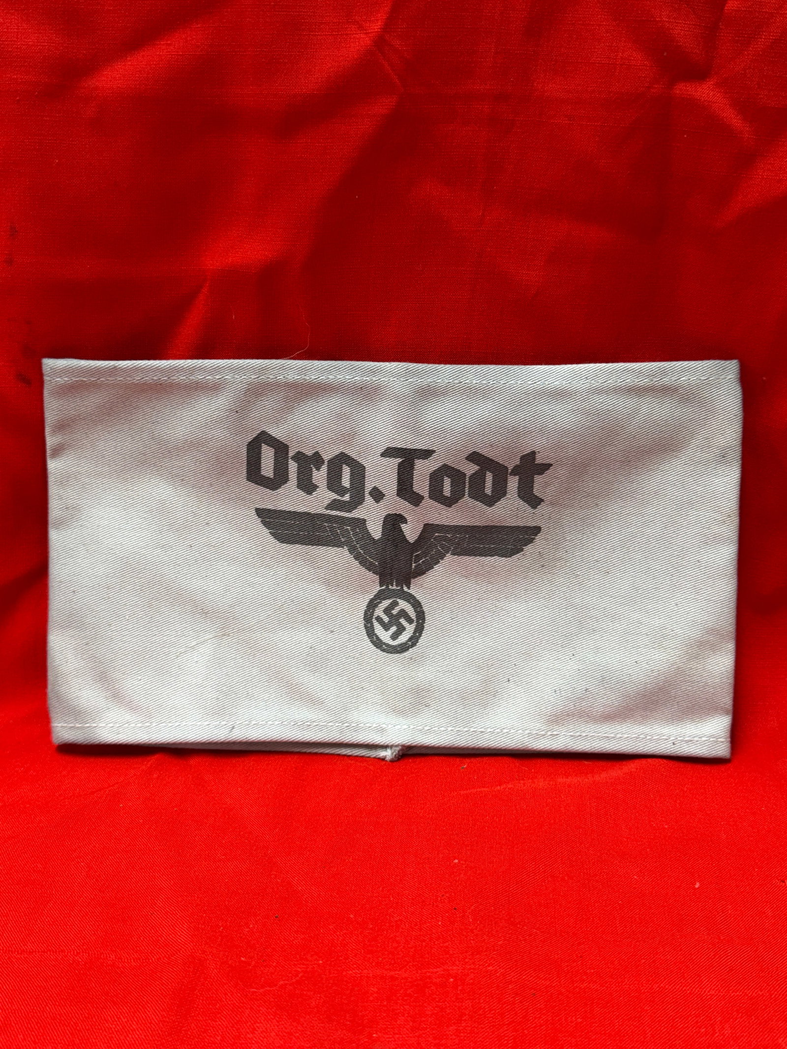 WW2 German Org. Todt Armband RZM Marked Civilian Organization Armband With RZM Paper Tag: WW2 German Org. Todt armband featuring printed “Org. Todt” script with eagle emblem on light colored cloth construction. Interior retains visible RZM style manufacturer label marked “Herstel