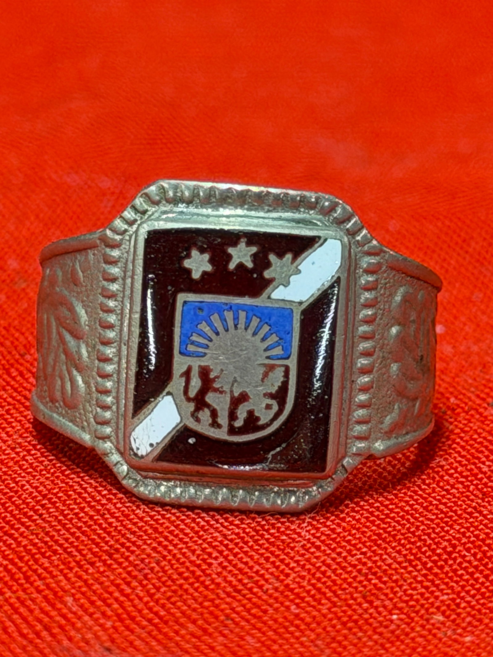 WW2 German Heraldic Enamel Ring Military Patriotic Style Ring: World War II era German patriotic style ring featuring a multicolor enamel heraldic crest design. The ring displays a shield with stylized coat of arms imagery, stars, and decorative side patterns in 
