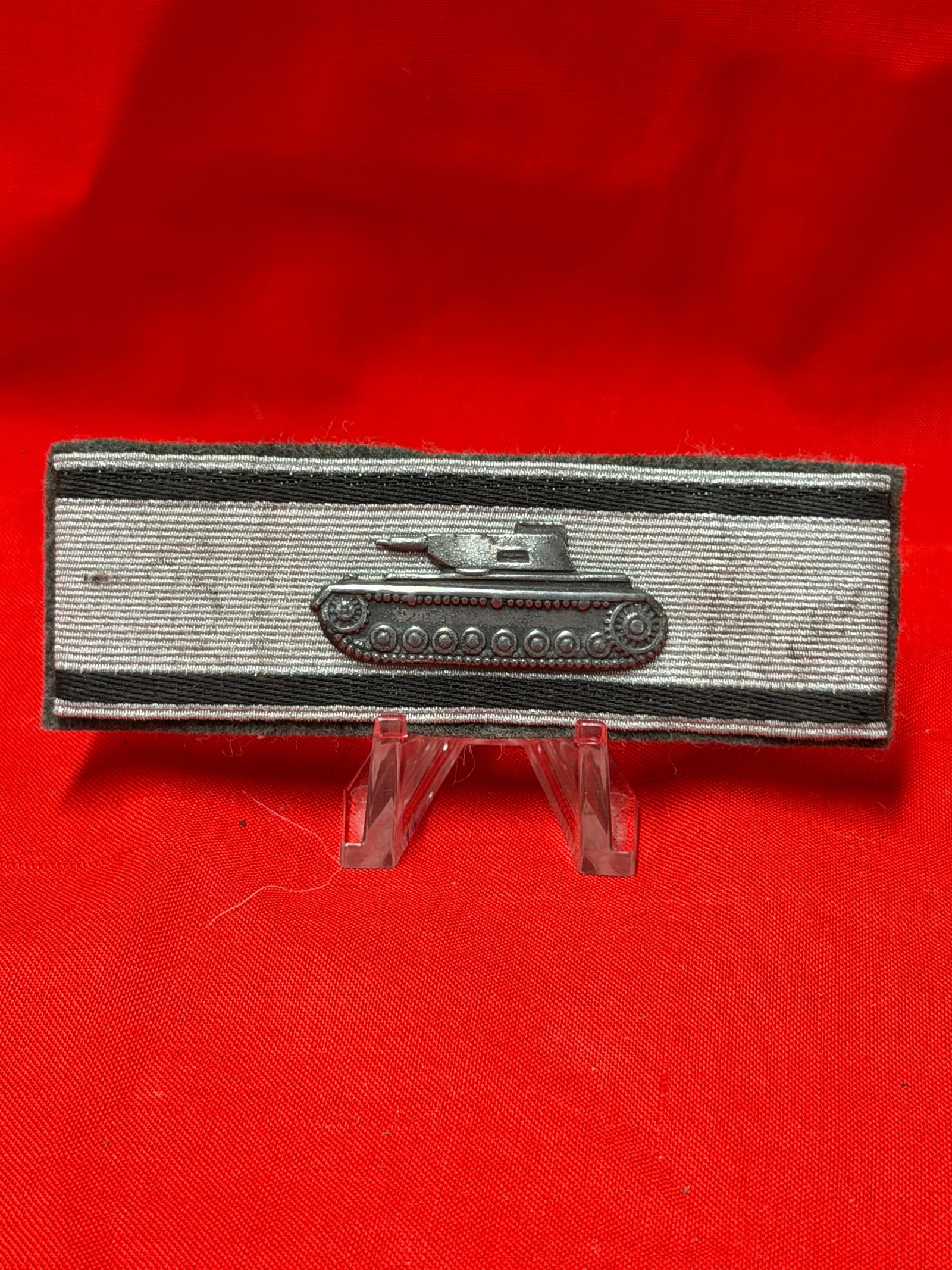 German WWII Style Panzer Shoulder Board With Tank Device: German military style shoulder board featuring silver woven trim with black stripe accents and attached metal tank insignia at center. Back side shows dark felt style material with visible age wear fr