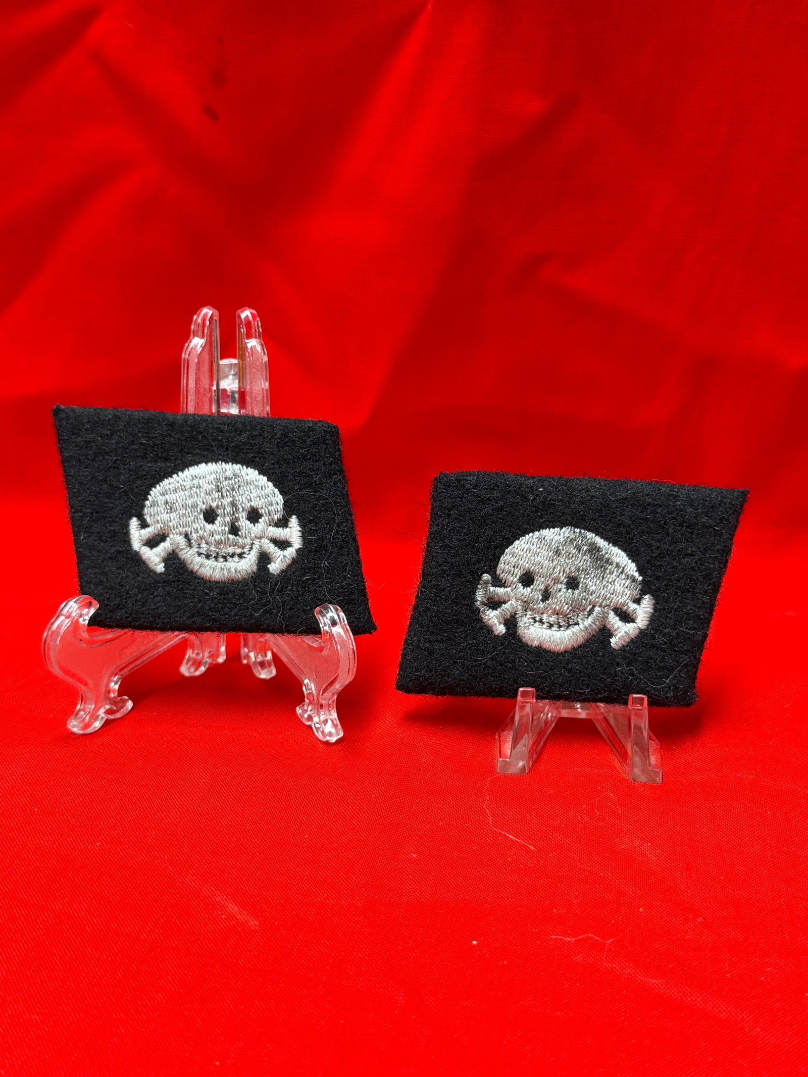 Pair of WWII German Skull Collar Tab Patches with RZM Tag: Matching pair of black cloth collar tab patches featuring embroidered skull and crossbones insignia. One tab retains original style paper RZM manufacturer tag on reverse. Items show age-related wear, 