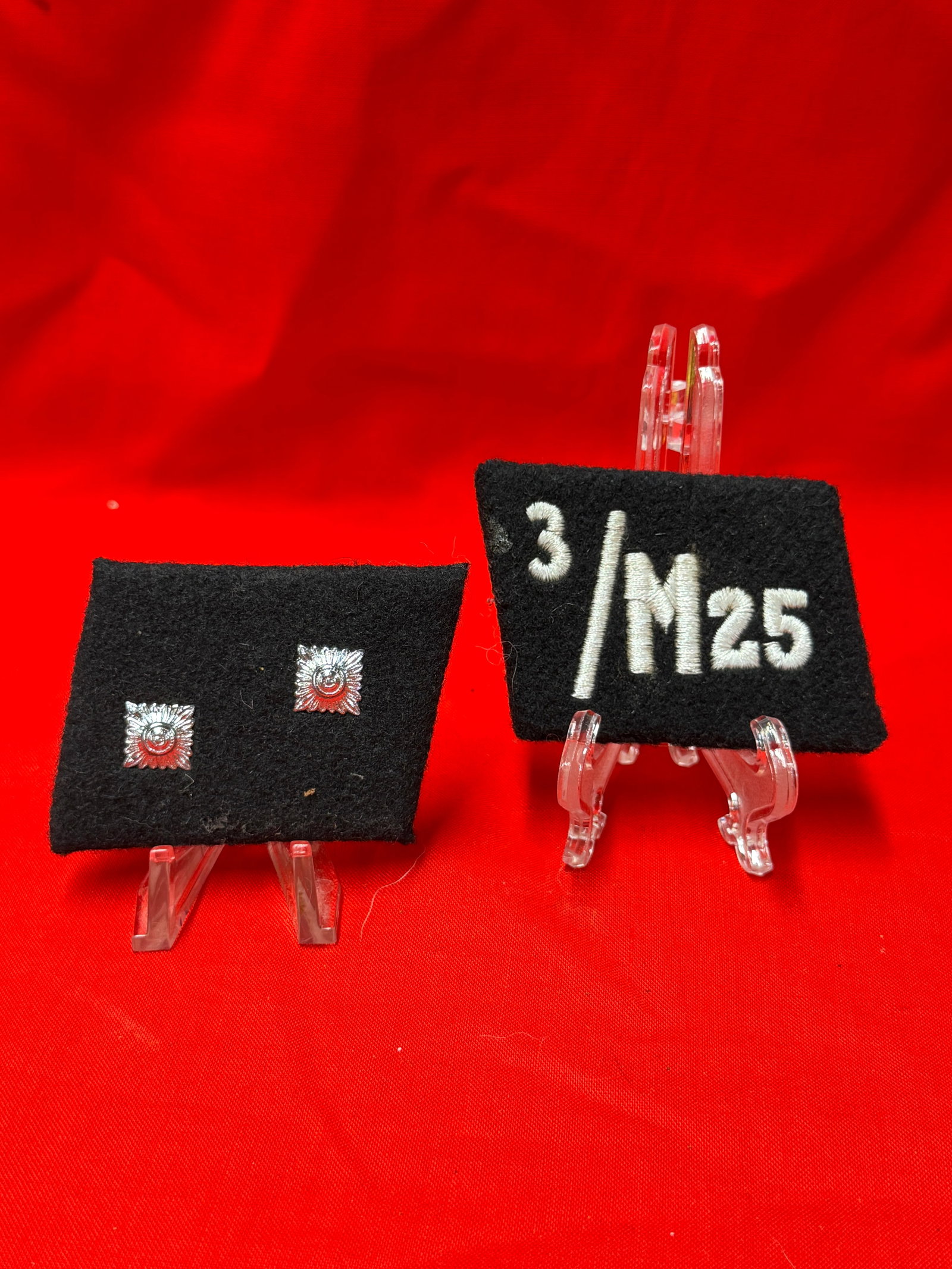 WWII German Waffen SS M25 Collar Tab Pair With Rank Insignia Tabs: Pair of black cloth collar tabs featuring embroidered “3/M25” insignia and silver-toned rank pips. Reverse side shows paper RZM manufacturer label and stitched backing details. In our opinion,