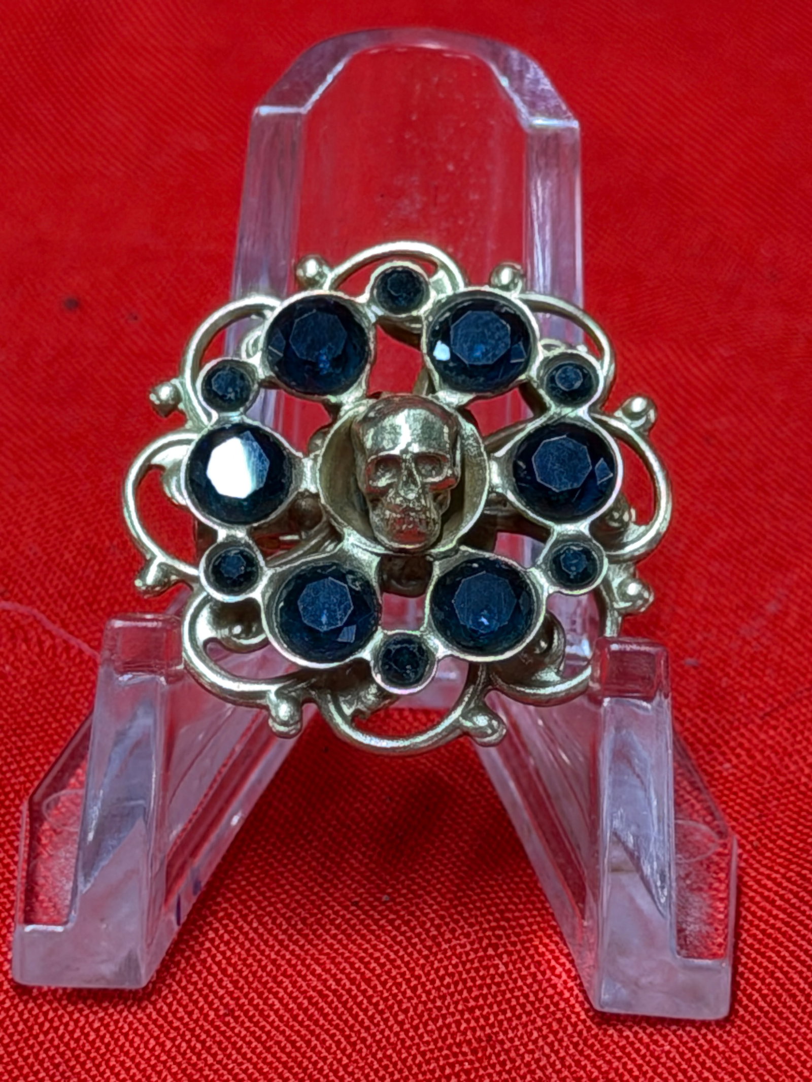 WW2 German Totenkopf Sweetheart Brooch With Skull And Blue Stones: Decorative sweetheart brooch featuring central Totenkopf skull motif surrounded by dark blue faceted stones in ornate circular setting. In our opinion, this piece appears to be inspired by German wart