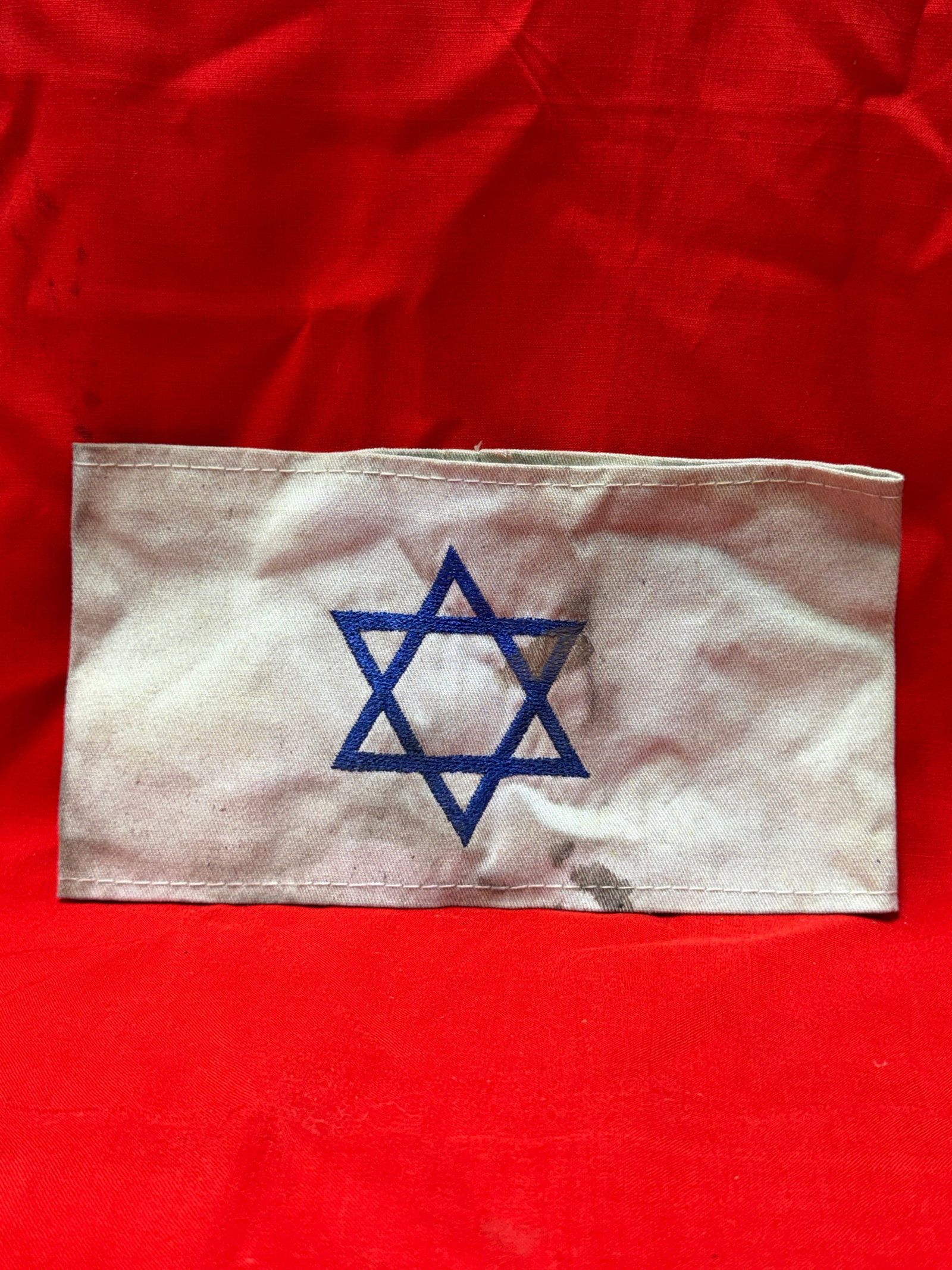 WWII German Jewish Star Of David Concentration Camp Armband: WWII German Jewish Star armband featuring a blue embroidered Star of David on a white cloth band with stitched edges and sewn construction throughout. In our opinion this piece represents a historical