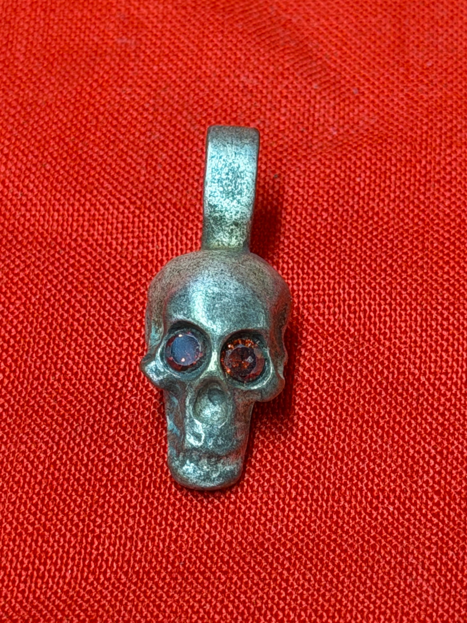 WWII German Totenkopf SS Death Head Skull Pendant w/ Red Stone Eyes: German WWII Totenkopf SS death head skull pendant featuring inset red glass or stone eyes and an aged darkened metal finish. The pendant displays detailed skull styling with integrated suspension loop