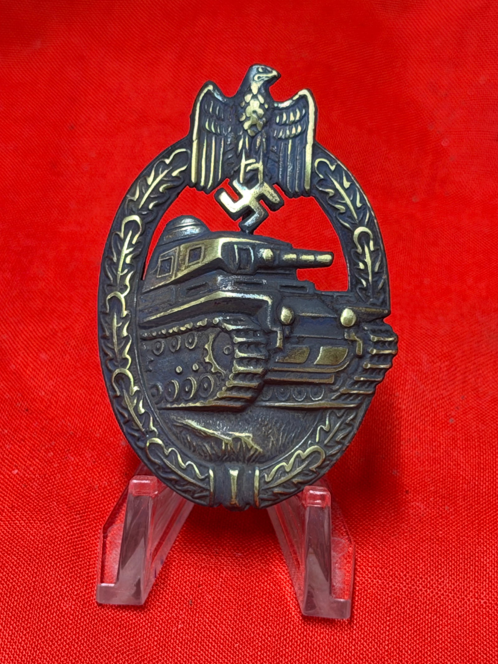 WW2 German Panzer Assault Tank Badge With Eagle Wreath Design Pinback Badge: German Panzer Assault badge featuring detailed tank design within oak leaf wreath surmounted by eagle emblem. Darkened metal construction with highlighted raised details throughout the tank, tracks, a