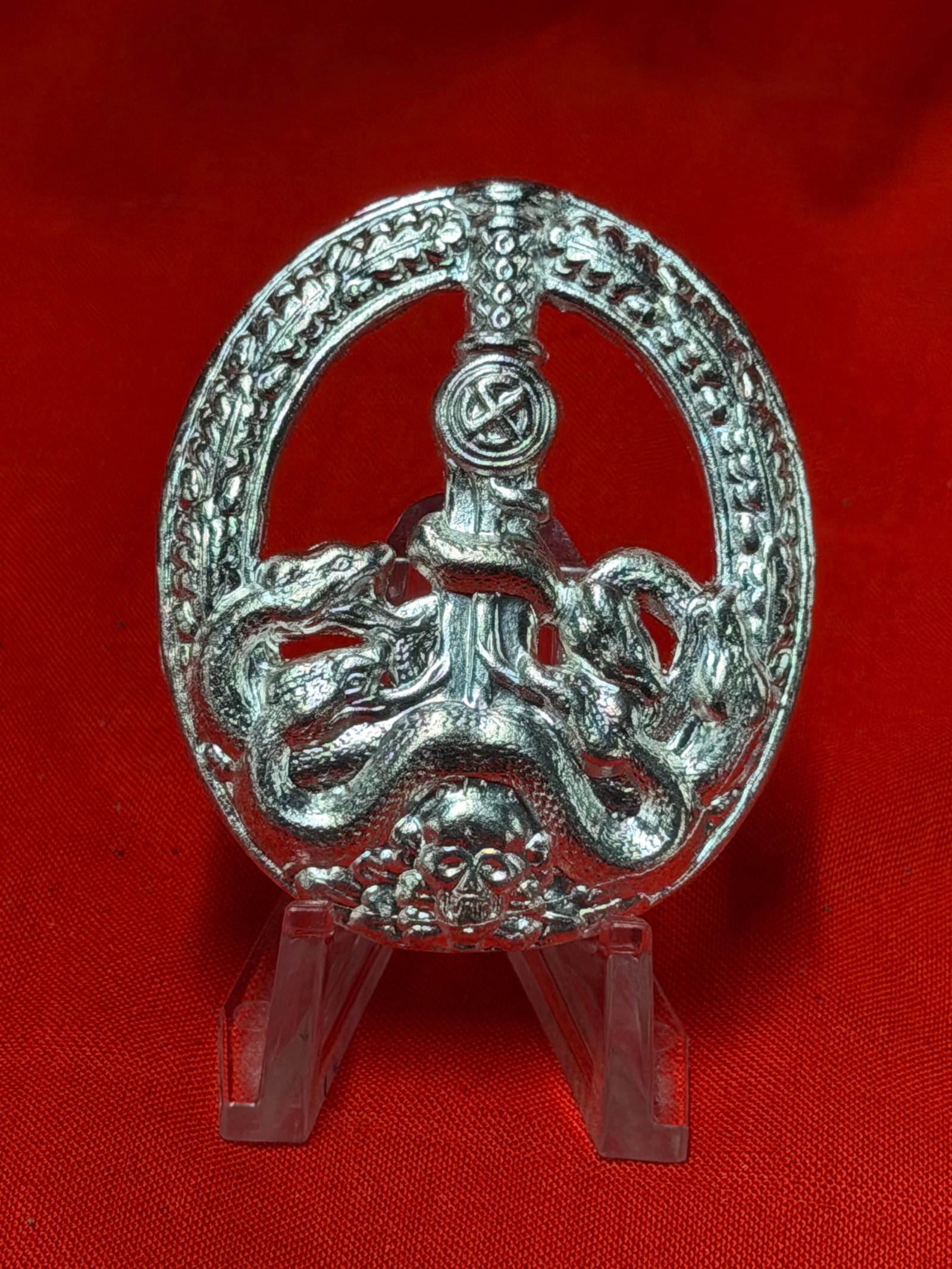 WW2 German Anti Partisan Badge Silver Tone Finish With Vertical Pin Back: WW2 German Anti Partisan related badge featuring circular wreath design with central sword, entwined serpent motif, and skull detail at base. Reverse retains vertical pin back assembly and textured re