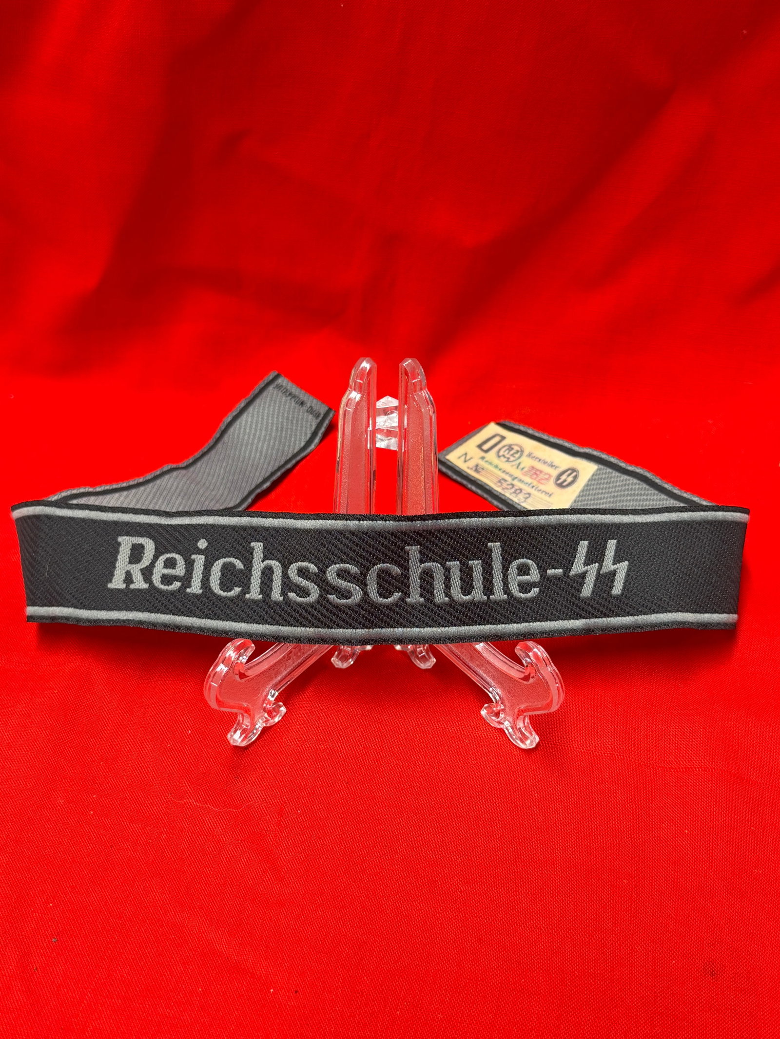 WW2 German Reichsschule SS Woven Uniform Cuff Title Armband Insignia With RZM Paper Tag: Black woven cuff title armband featuring Reichsschule-SS script lettering with silver tone border trim and maker markings visible on the reverse side. In our opinion this is an interesting German mili