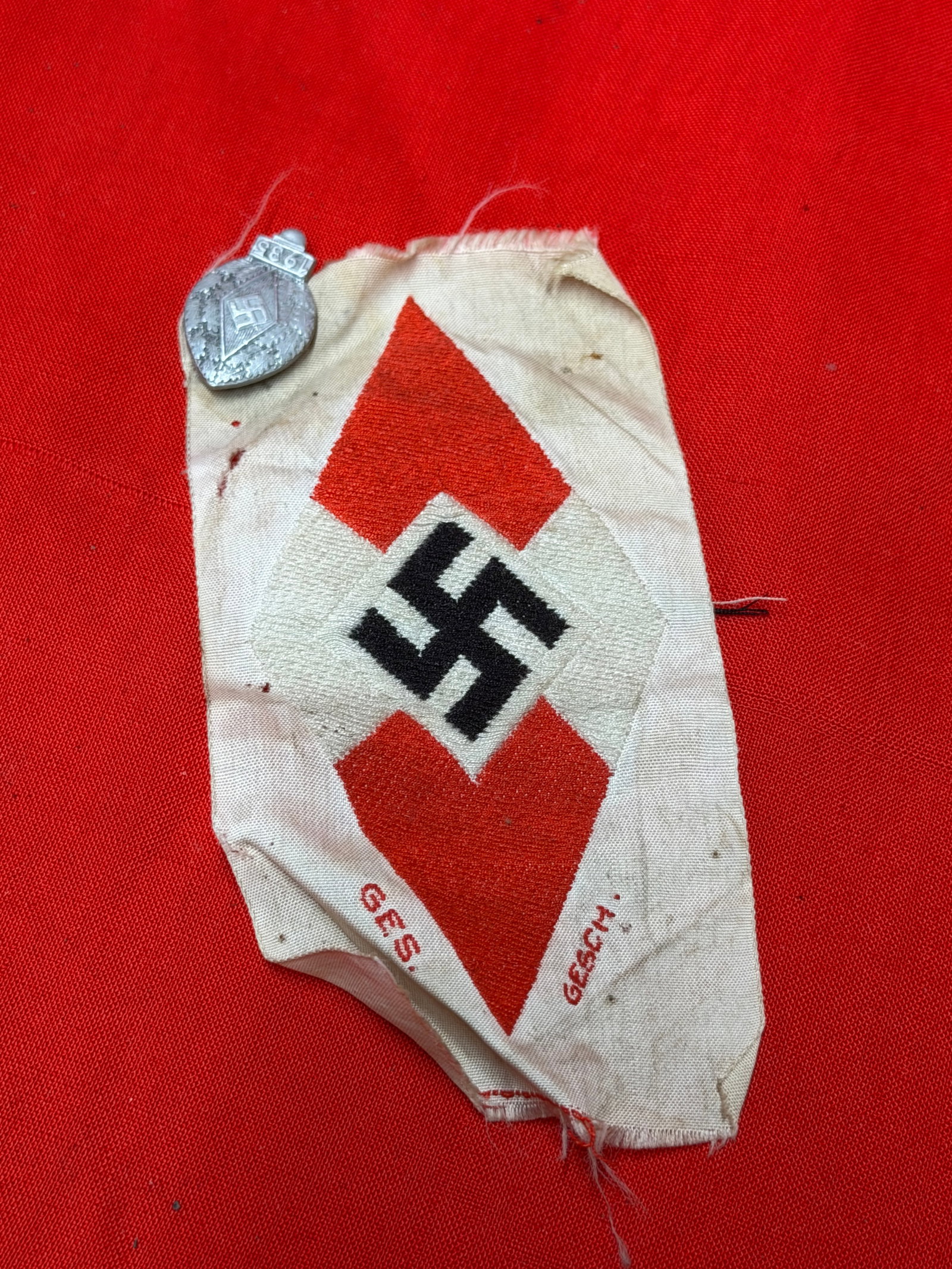 WWII German Hitler Youth Sleeve Patch with Attached 1935 Membership Pin: WWII German Hitler Youth sleeve patch featuring the traditional black swastika on white and red diamond insignia sewn to a cloth backing. Includes an attached 1935 dated Hitler Youth membership style 