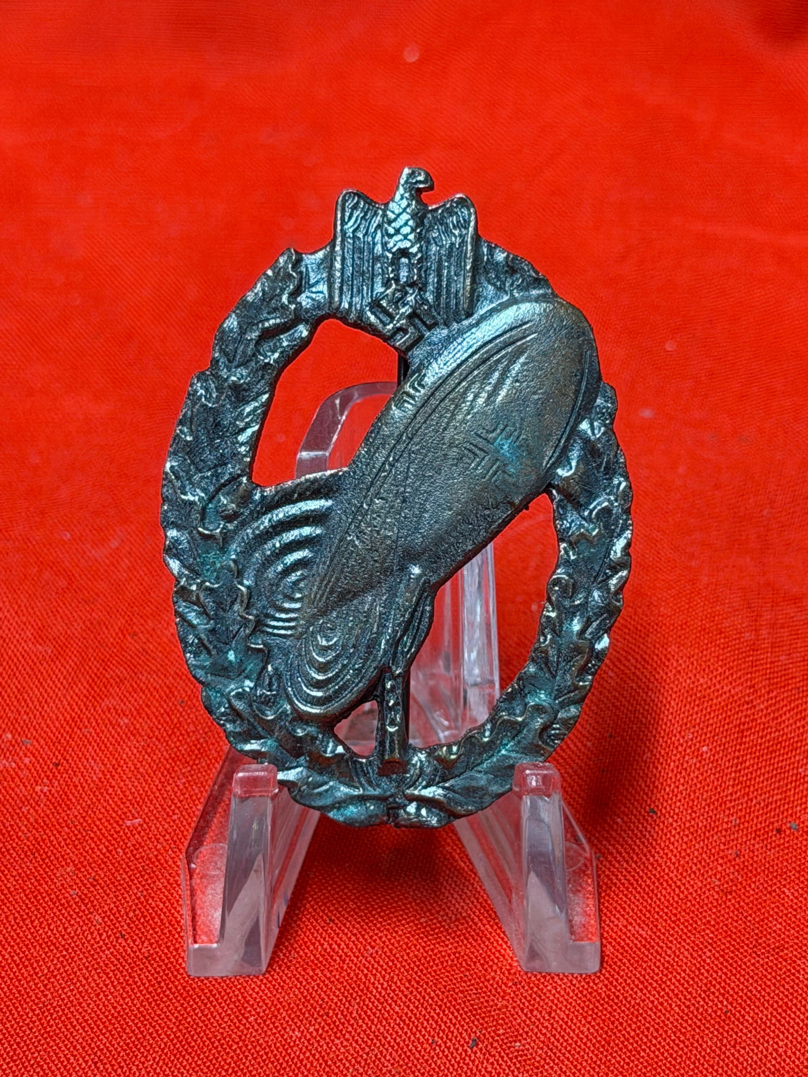 German WWII Style Airship / Zeppelin Badge Pin – Metal Wreath Design: German WWII style airship / zeppelin themed badge featuring a dirigible design set within an oak leaf wreath topped by an eagle emblem. Constructed of darkened metal with pinback fastener on the rever
