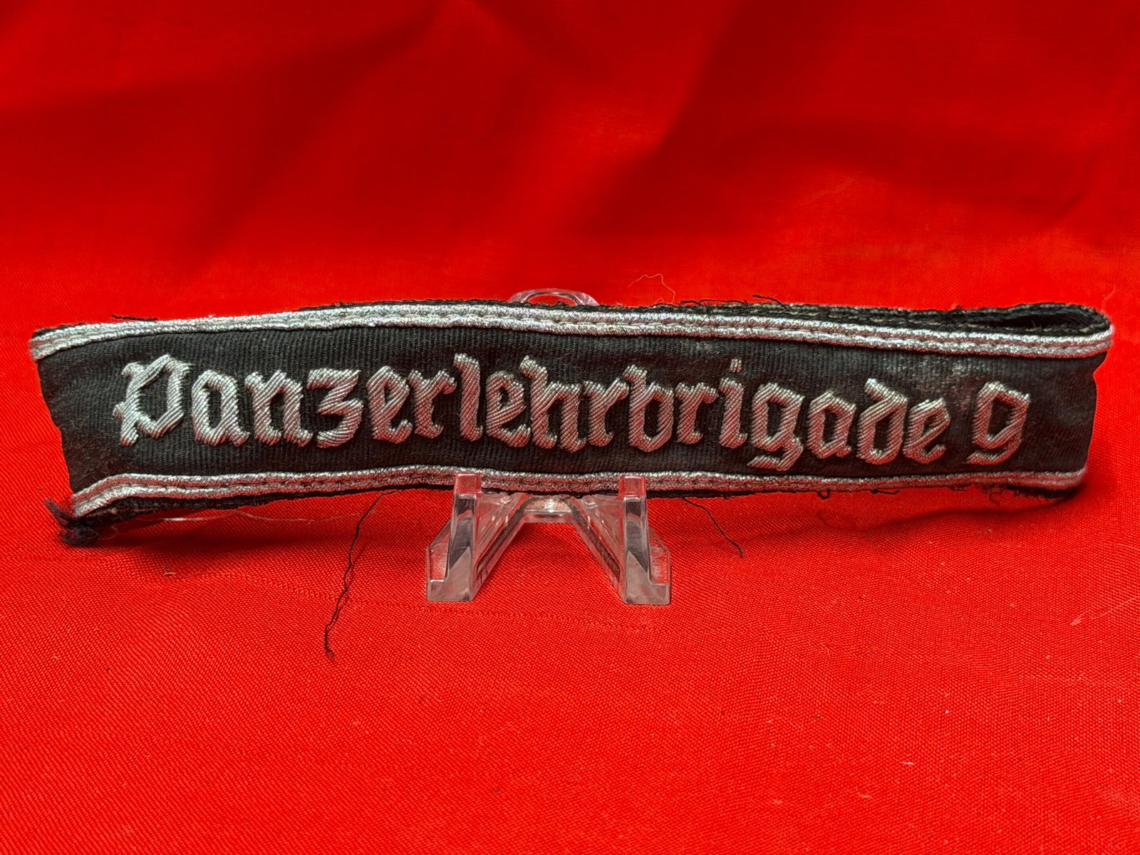 WWII German SS Panzer “Panzerlehrbrigade?? Cuff Title Armband: WWII German Waffen-SS style cuff title embroidered “Panzerlehrbrigade” in silver-gray script on a black woven band with silver edge piping. Constructed in the traditional tubular style for wea