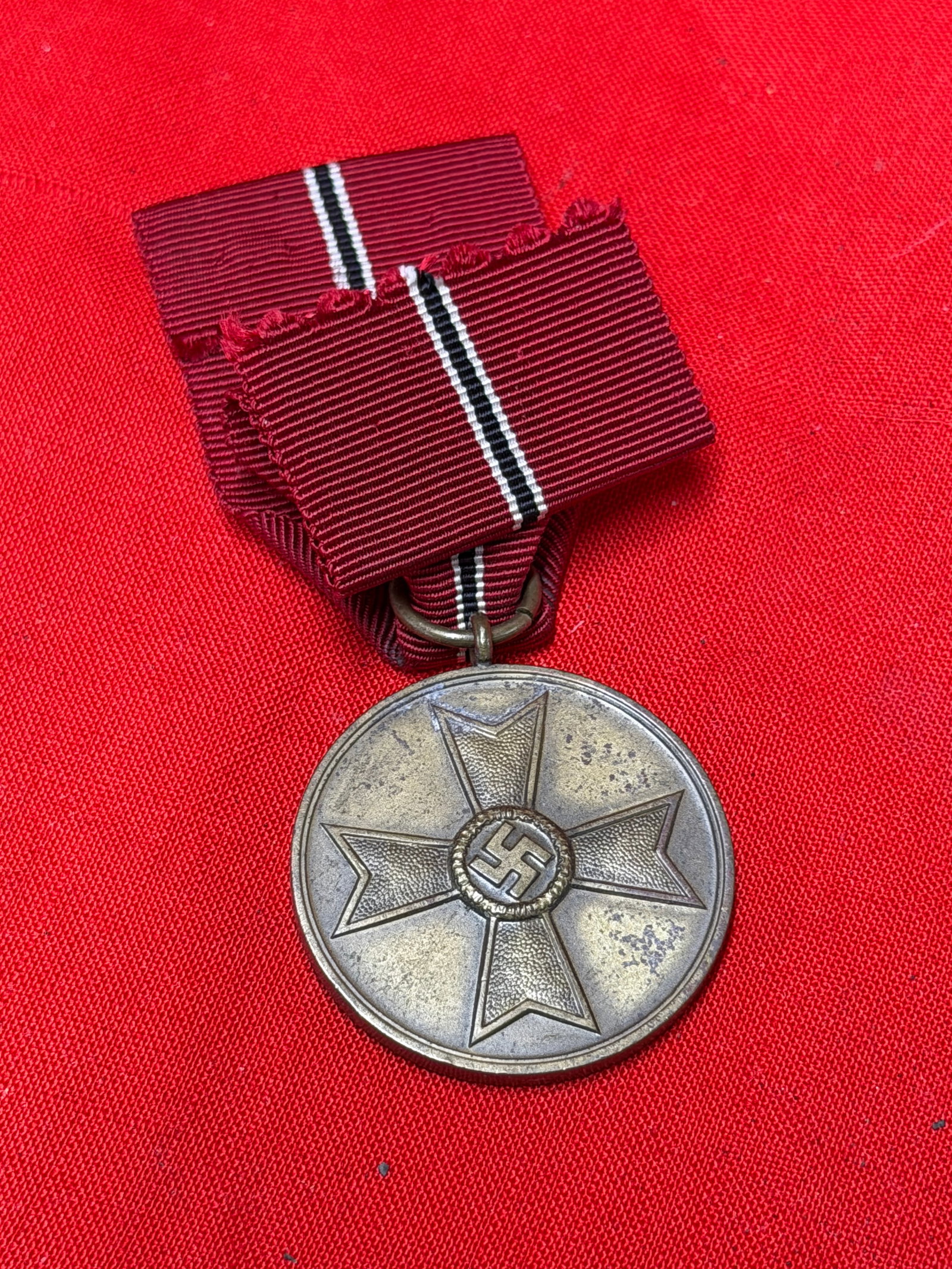 WWII German War Merit Medal 1939 (Kriegsverdienstmedaille) with Ribbon: WWII German War Merit Medal (Kriegsverdienstmedaille 1939) complete with its red ribbon featuring black-and-white center stripes. The obverse displays the War Merit Cross design with central wreath an