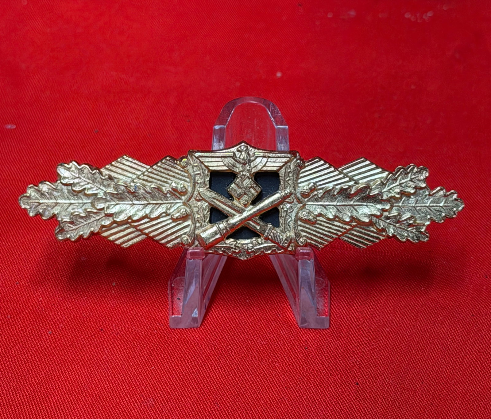 WWII German Close Combat Clasp Crossed Weapons Badge Pin R.S.&S. Marked: WWII German close combat clasp badge featuring crossed weapons beneath an eagle emblem with oak leaf wreath accents and dark center panel. Gold-tone finish with horizontal pinback attachment on revers