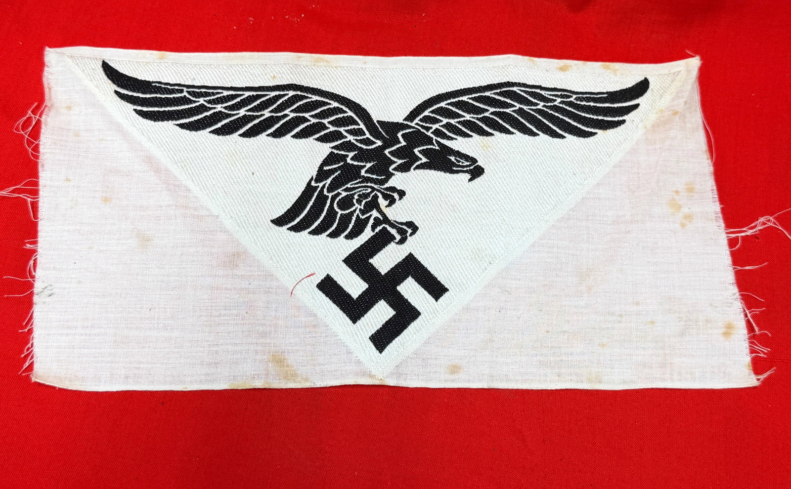 WWII German Luftwaffe Eagle Cloth Uniform Insignia Patch Panel: German Luftwaffe related cloth insignia panel featuring black and white eagle with swastika emblem on triangular woven backing attached to white fabric strip. Measures approximately 10 inches across o