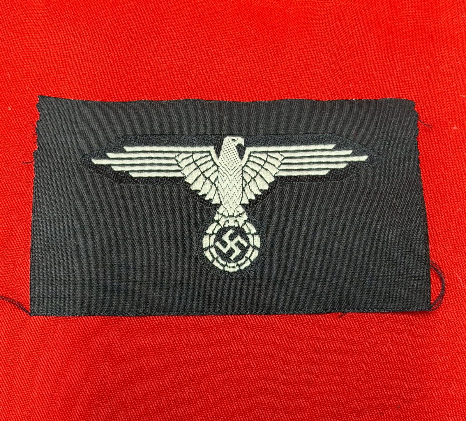 WWII German Waffen-SS BeVo Sleeve Eagle Insignia Patch: Second World War German Waffen-SS BeVo woven sleeve eagle insignia featuring silver-gray eagle and swastika on black rayon backing. Reverse displays characteristic BeVo style horizontal weave construc