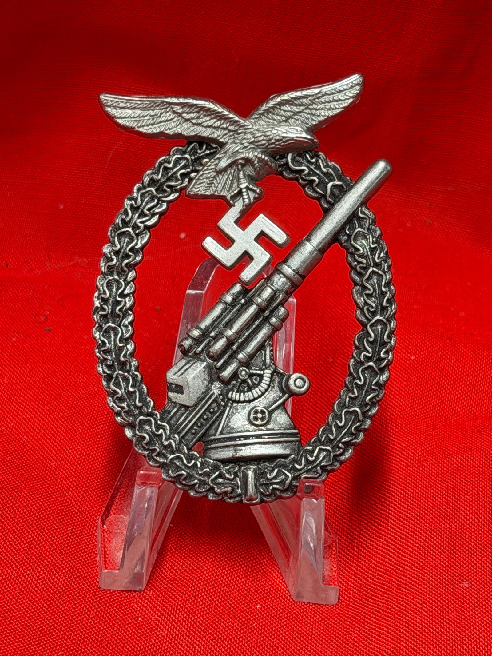 WWII German Luftwaffe Flak Badge – Anti-Aircraft Artillery Award: Second World War German Luftwaffe Flak Badge featuring Luftwaffe eagle, swastika, and anti-aircraft artillery gun within oakleaf wreath. Constructed in silver-tone metal with vertical pinback setup to