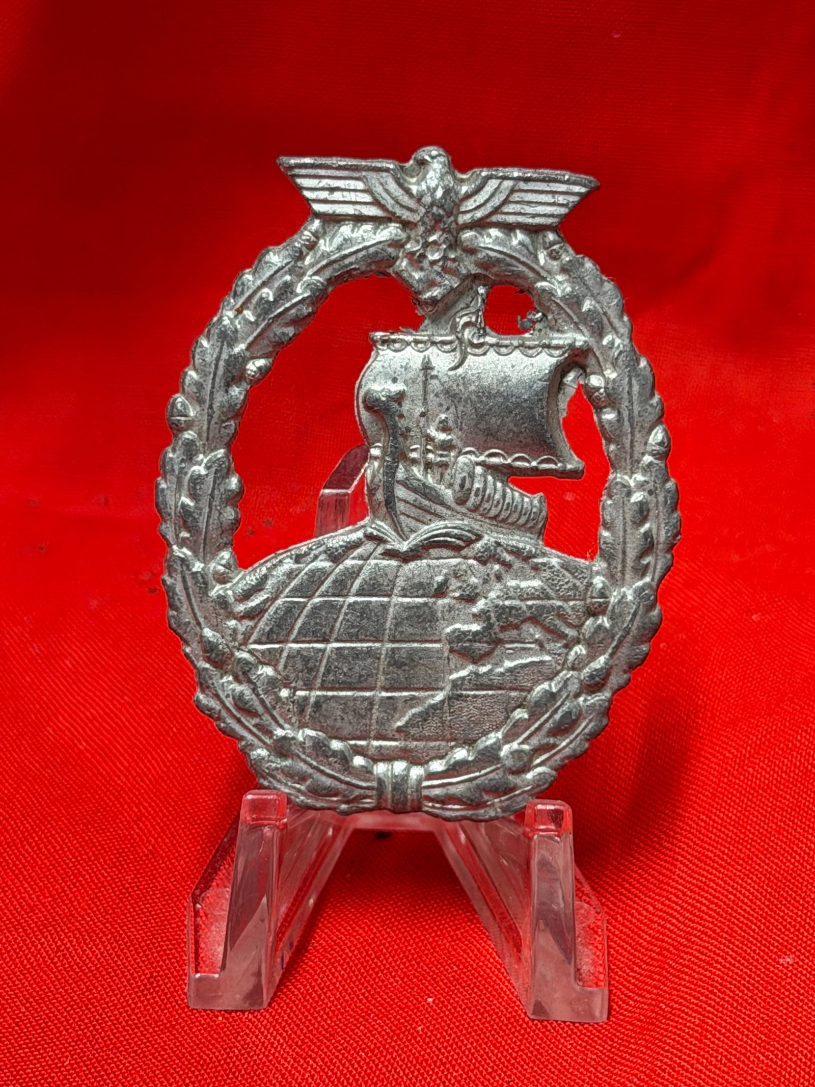 WWII German Kriegsmarine Auxiliary Cruiser War Badge: This Second World War German Kriegsmarine Auxiliary Cruiser War Badge features detailed globe, Viking ship, oakleaf wreath, and eagle design in silver-tone metal. In our opinion the badge displays per