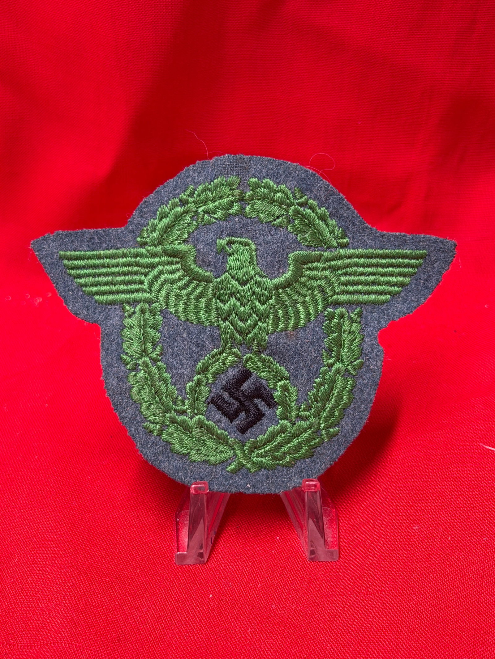 WWII German Police Sleeve Eagle Patch: This Second World War German Police sleeve eagle patch features green embroidered eagle and oakleaf wreath design on gray wool backing with black swastika detail. In our opinion the patch displays per