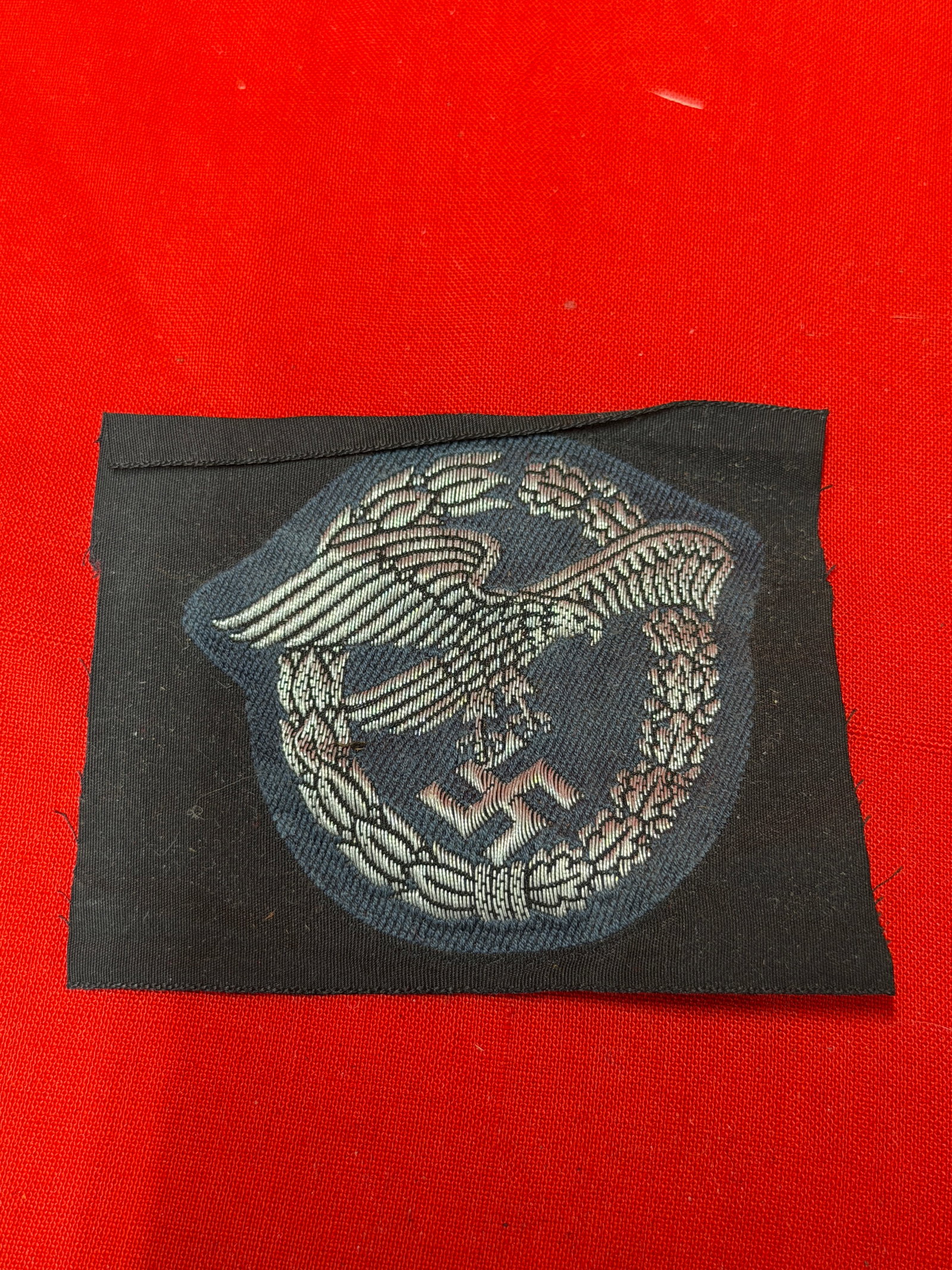 WWII German Luftwaffe Cloth Observer Badge Patch – Machine Embroidered Insignia: WWII era German Luftwaffe cloth Observer Badge patch featuring a silver-gray embroidered eagle in flight with swastika surrounded by an oakleaf wreath on blue-gray wool backing. Machine embroidered co