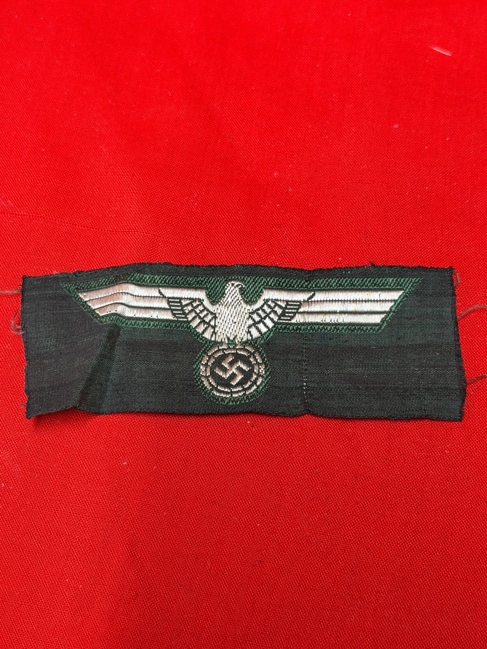 WWII German Heer Army Breast Eagle Insignia Patch – Machine Embroidered BeVo Style: WWII era German Heer (Army) breast eagle insignia patch featuring a silver-gray eagle clutching a wreathed swastika embroidered on dark field backing with dark green accent stitching. Machine embroide