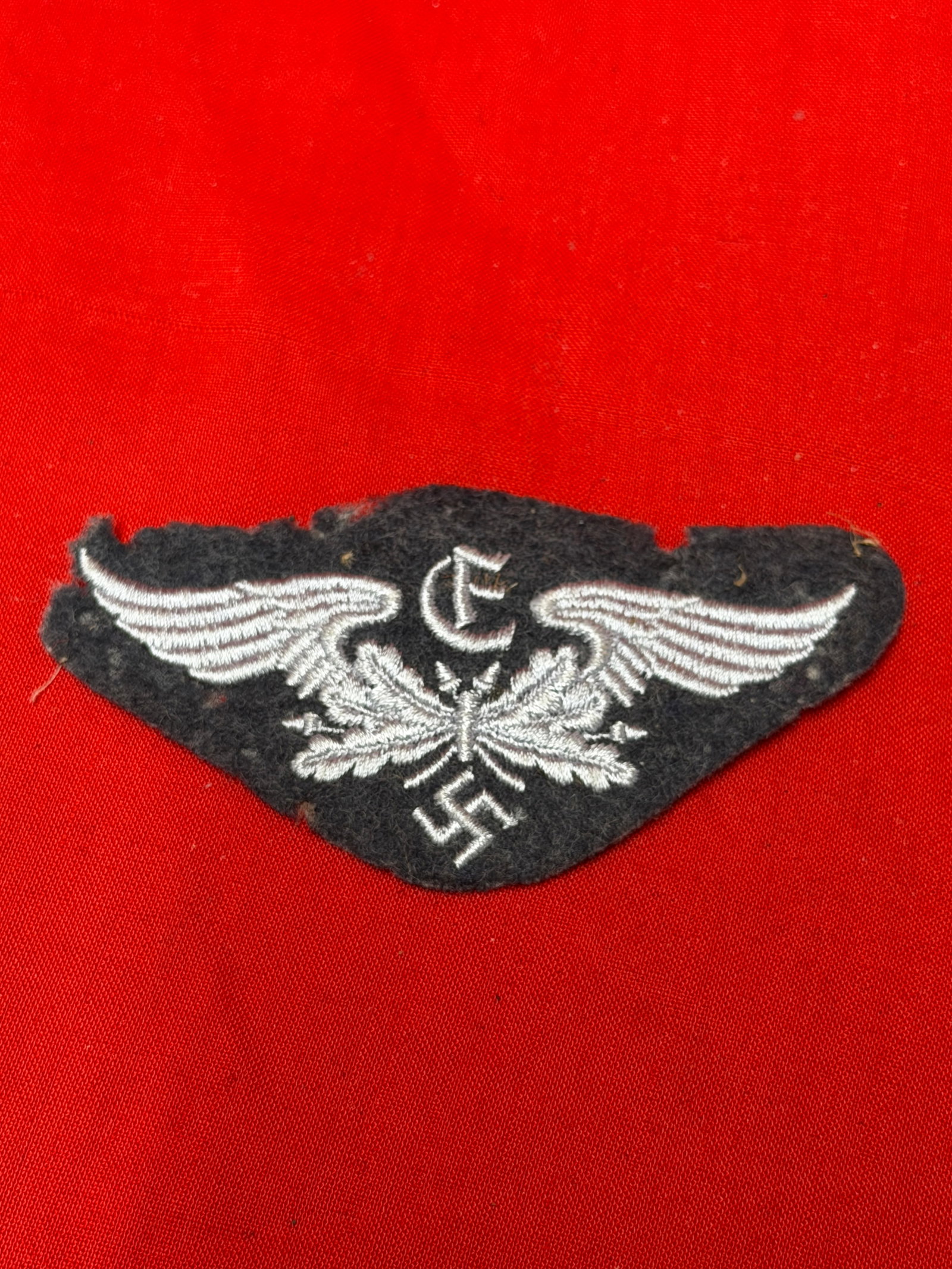 WWII German Third Reich Luftwaffe-Style Cloth Insignia Patch: Vintage World War II era German Third Reich Luftwaffe-style embroidered cloth insignia patch featuring spread wings, oak leaves, and central symbol embroidered in white thread on black wool backing. T