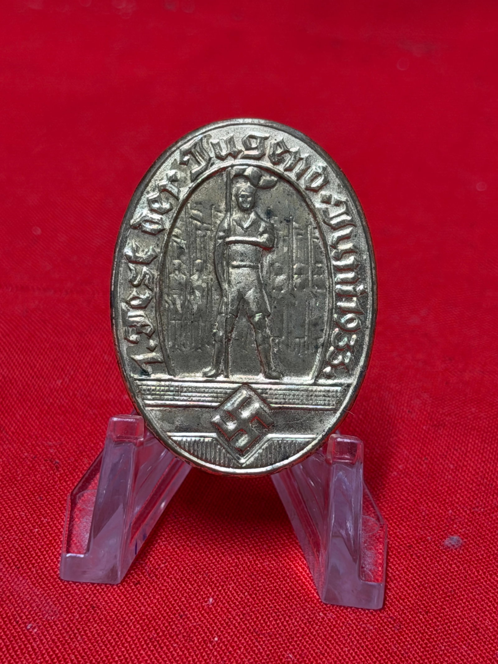 1933 German Hitler Youth Fest Der Jugend Tinnie Badge: June 1933 German Hitler Youth “Fest Der Jugend” tinnie badge featuring standing youth figure with surrounding German text and lower emblem detail. In our opinion, the piece is constructed from