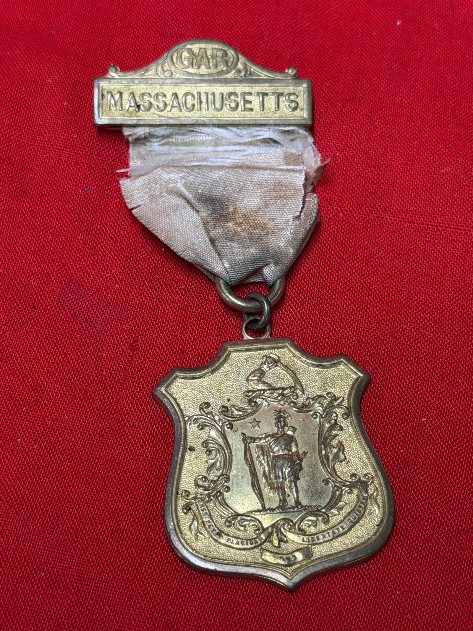 Antique G.A.R. Massachusetts Civil War Veteran Medal Badge – Grand Army of the Republic Ribbon Pin: Antique Grand Army of the Republic (G.A.R.) Massachusetts department veteran badge featuring an ornate shield-shaped pendant with the Massachusetts state seal and “Massachusetts” top bar. Reve