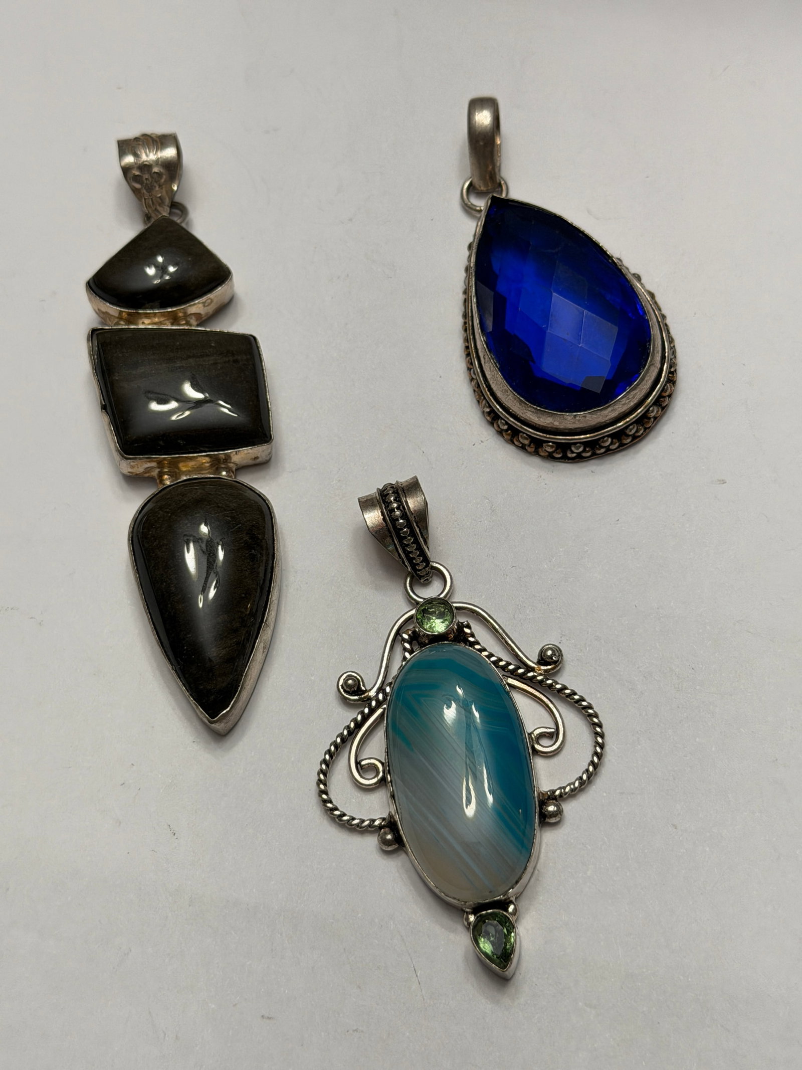 Vintage Sterling Silver Pendant Lot Blue Glass Agate Obsidian Artisan Jewelry Collection: Collection of three vintage sterling silver pendants featuring unique artisan gemstone and glass designs. Includes a faceted cobalt blue teardrop pendant, an ornate blue banded agate style pendant wit
