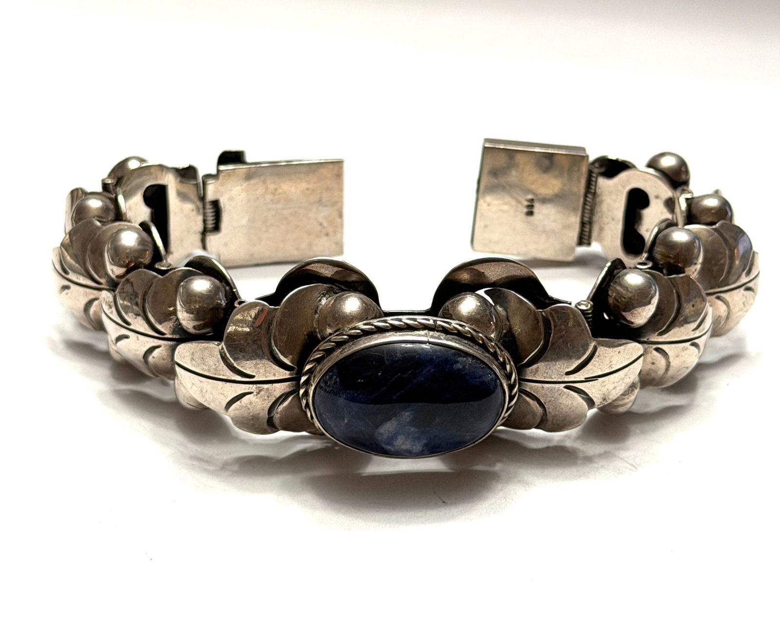 Vintage Sterling Silver 980 Blue Stone Bracelet Taxco Style Statement Cuff: Beautiful vintage sterling silver bracelet featuring a deep blue oval cabochon stone centerpiece in an ornate handcrafted Taxco style design. Marked 980 silver on clasp indicating high silver purity. 
