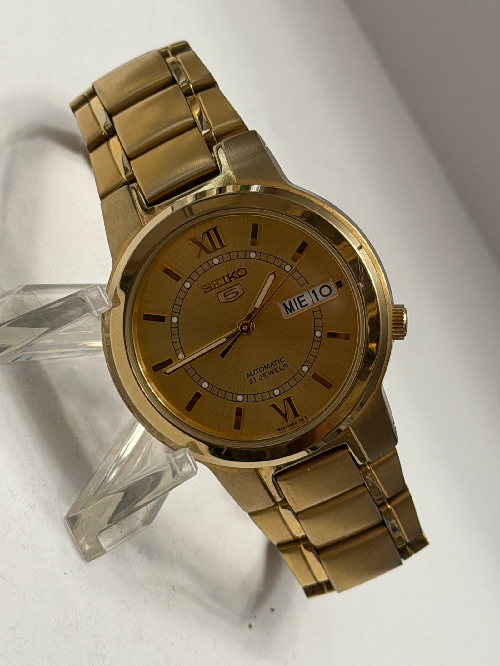 Seiko 5 Automatic 21 Jewels Gold Tone Day-Date Men?s Watch Display Case Back: Elegant Seiko 5 Automatic men’s wristwatch featuring a full gold-tone stainless steel case and matching bracelet with a classic champagne dial. This timeless automatic timepiece includes a bilin
