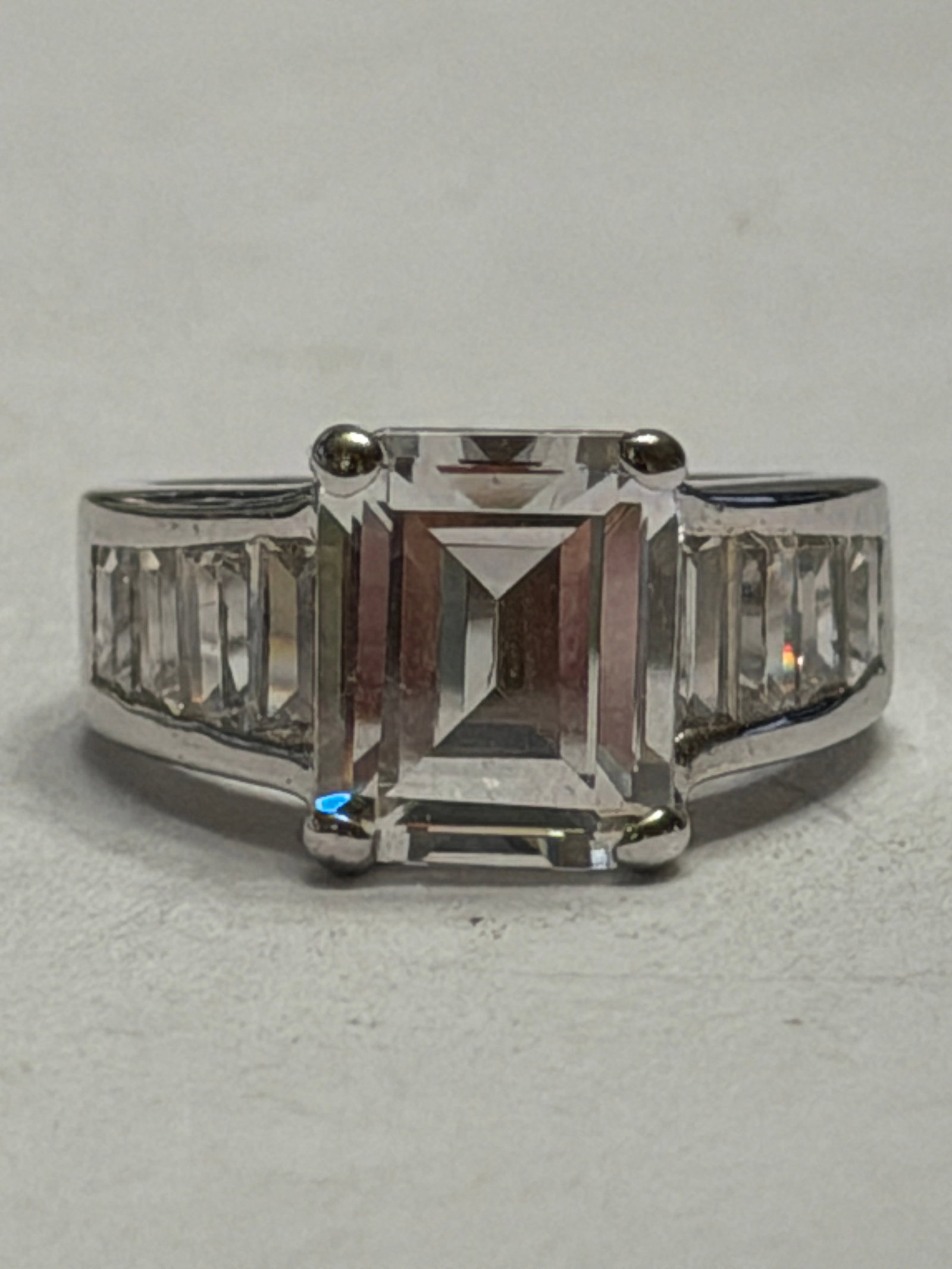 Sterling Silver Emerald Cut CZ Ring with Channel Set Accents ? Size 6: Sophisticated sterling silver statement ring featuring a large emerald-cut clear center stone in a classic four-prong setting. The shoulders of the wide polished band are accented with channel-set bag