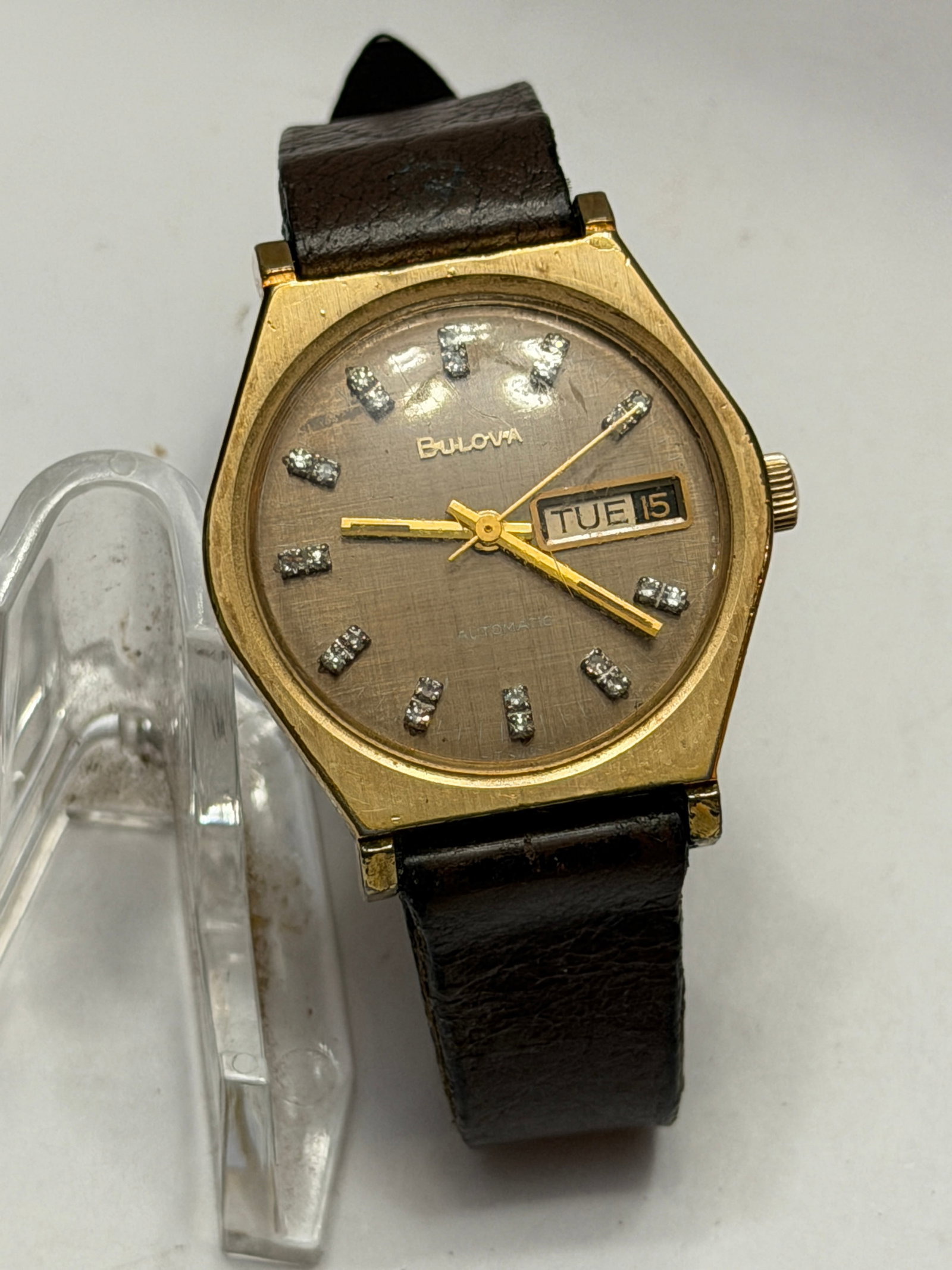 Bulova Automatic Day-Date Wristwatch ? Gold Tone w/ Textured Dial & Diamond Accent Markers: Classic vintage Bulova automatic day-date wristwatch featuring a distinctive 1970s angular gold-tone case and an elegant textured champagne/taupe dial accented with sparkling stone-set hour markers. T
