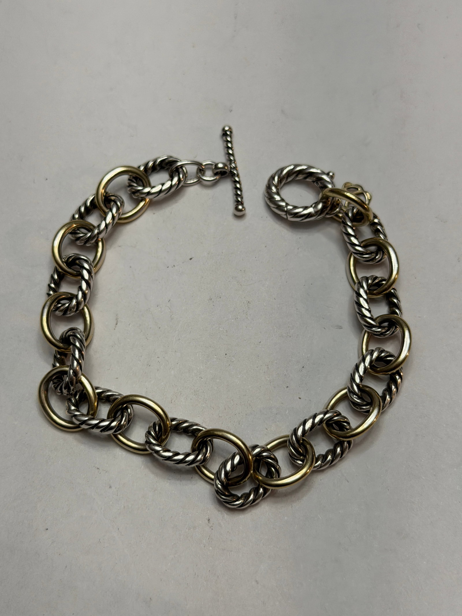 David Yurman Sterling Silver & 18K Gold Cable Link Bracelet: Authentic David Yurman bracelet crafted in the brand’s iconic mixed-metal style, featuring richly textured sterling silver cable links accented with elegant 18K yellow gold rings throughout the 