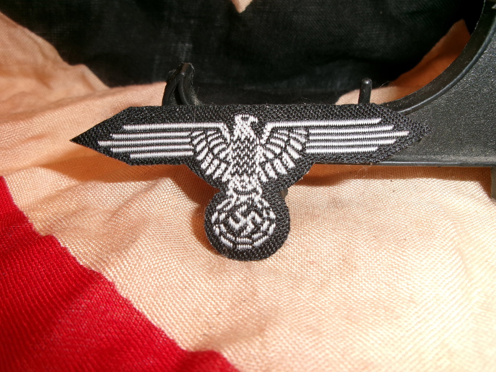 WWII German National Eagle Cloth Uniform Insignia: This embroidered German national eagle insignia is woven in silver-gray thread on black cloth backing and depicts the stylized spread-wing eagle clutching a wreath enclosing a swastika. Uniform breast