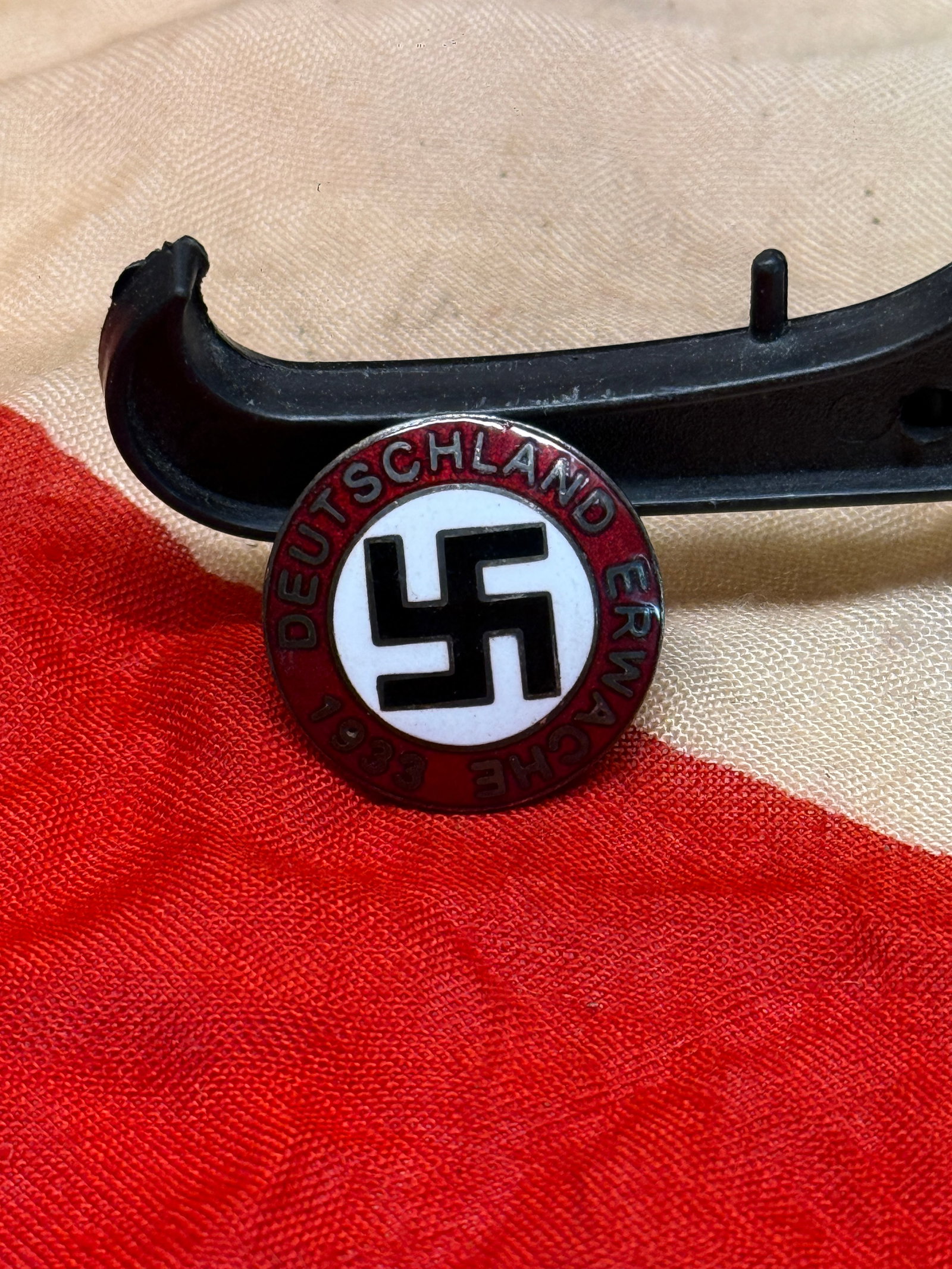 WWII German “Deutschland Erwache?? Membership Badge By RZM M/129: This circular red, white, and black enamel badge bears the inscription “Deutschland Erwache 1933” surrounding a central swastika emblem. The reverse includes fastening hardware and stamped mar