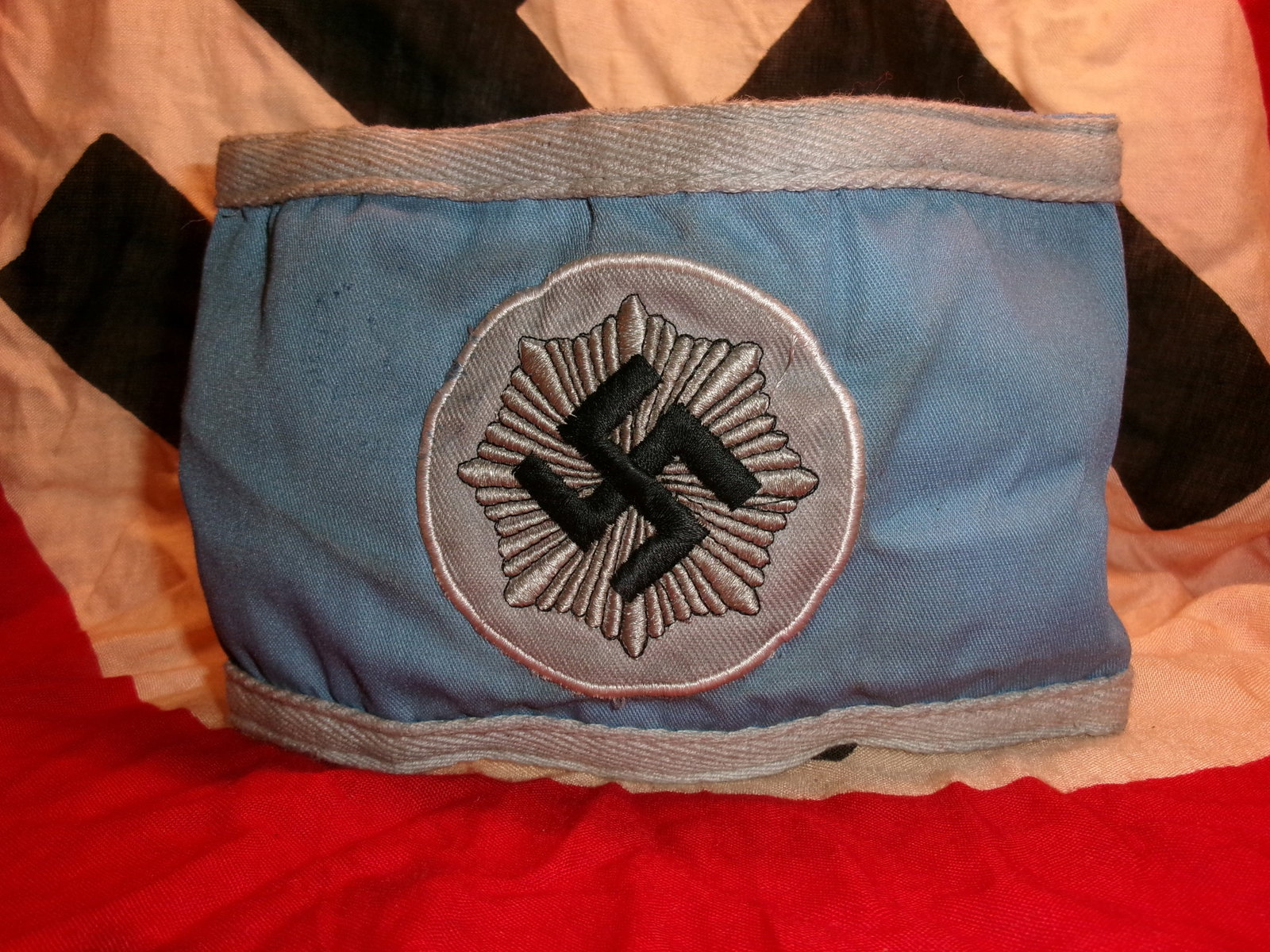 WWII German Reichsluftschutzbund (RLB) Second Pattern Cotton Armband: This WWII-era German armband is identified as a second-pattern Reichsluftschutzbund (RLB) cotton armband, produced in blue cloth with grey border trim and a centrally applied silver-grey radiating emb