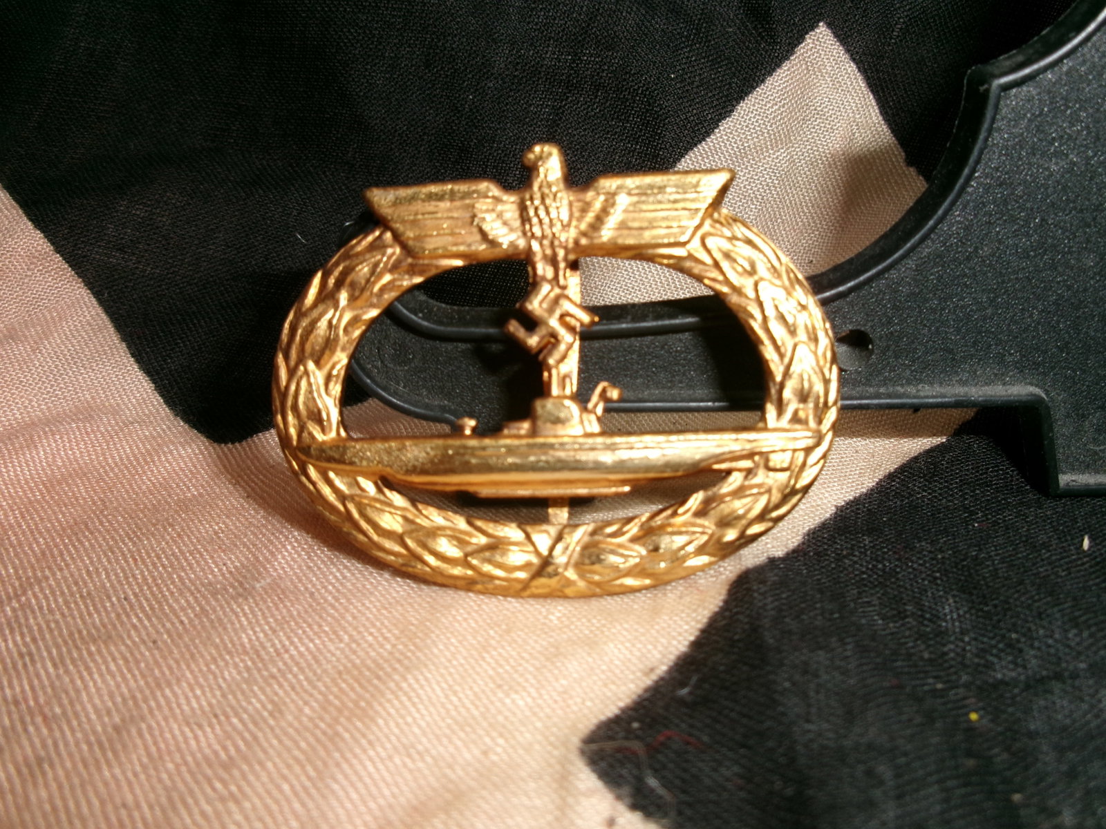 WWII German Kriegsmarine U-Boat Submarine Warfare Badge Style Gold Tone Pin: WWII German Kriegsmarine U-Boat submarine warfare badge style pin featuring a submarine beneath an eagle within an oak leaf wreath. Gold tone construction with a horizontal pin-back attachment on the 