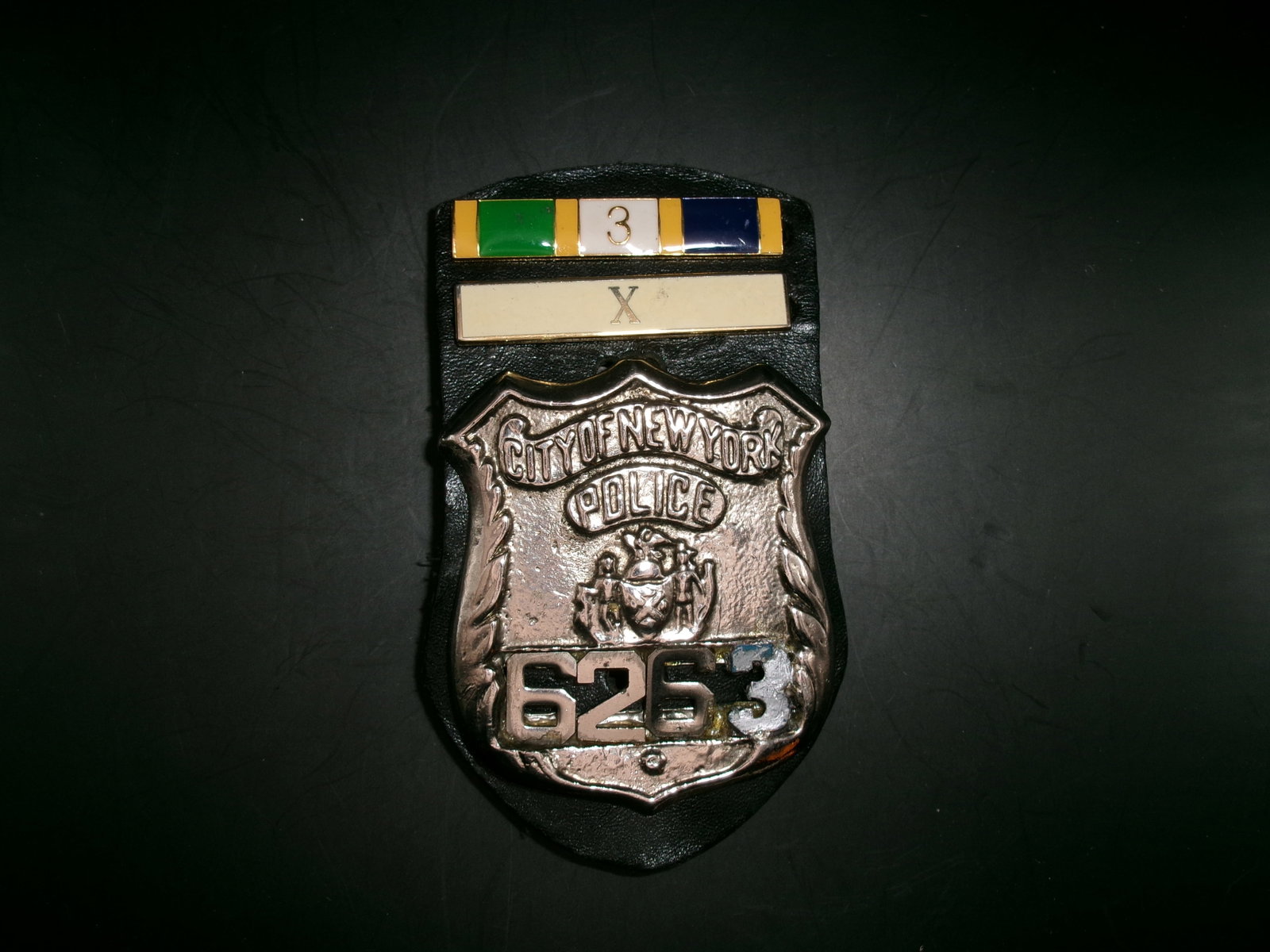Modern New York City Police Department Detective Shield Presentation Badge: Decorative New York City Police Department-style detective shield mounted on a black leather presentation backing with multicolor service-style ribbon bars and Roman numeral “X” insignia plate