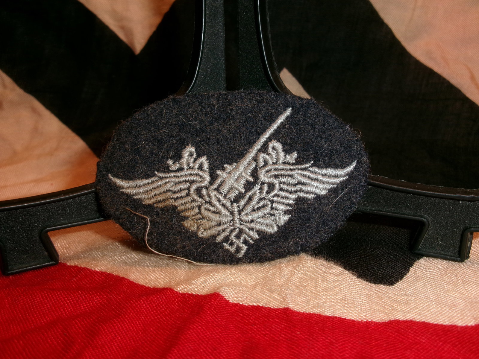 WWII German Luftwaffe Embroidered Qualification Breast Insignia: Oval dark wool-backed embroidered insignia displaying a silver-gray winged eagle superimposed with an upright sword motif, representative of a Luftwaffe qualification or specialist designation from th