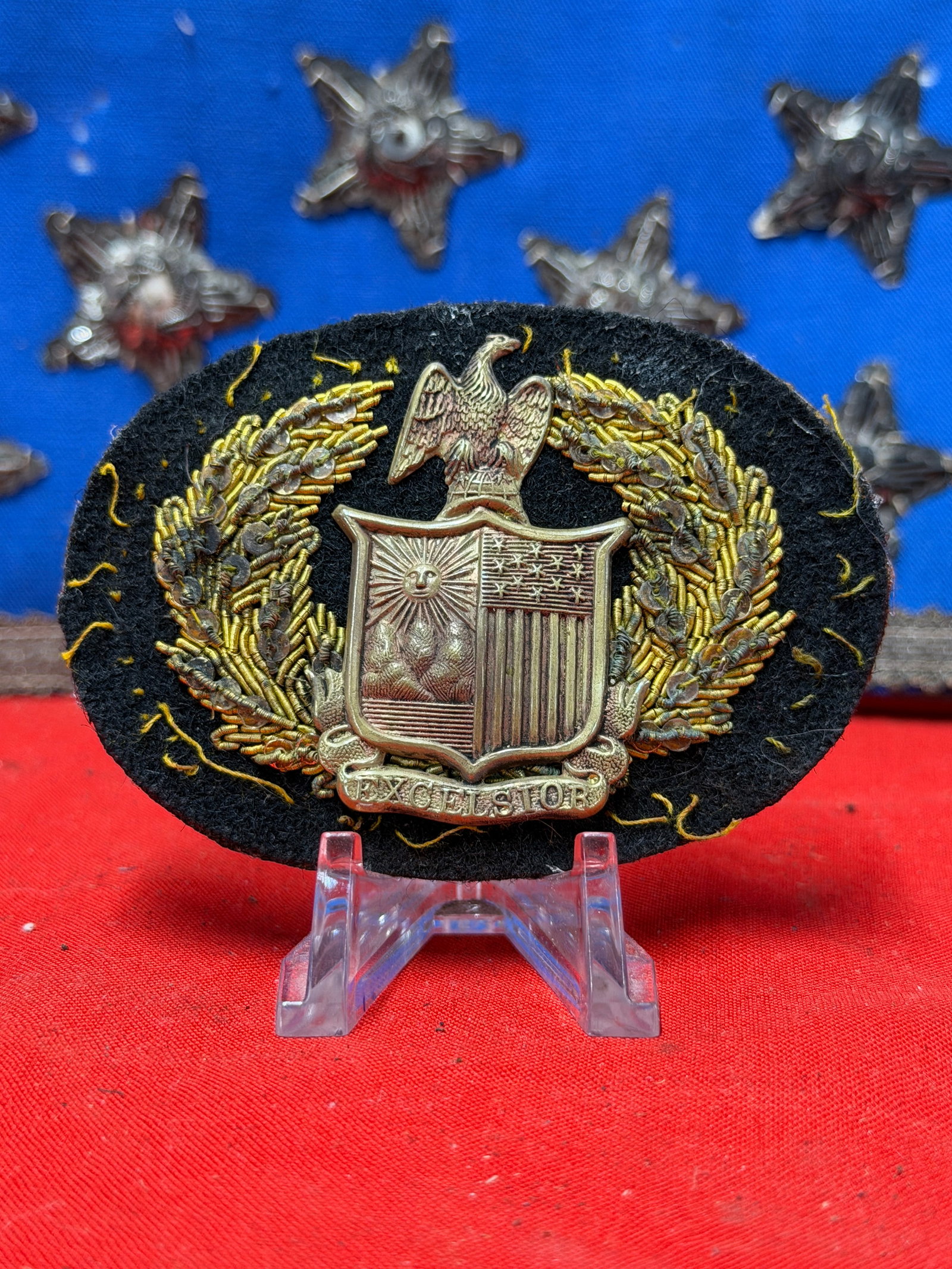Civil War Era New York Excelsior Bullion Headgear Badge by Schuyler, Hartley & Graham: Offered is a Civil War-era New York Excelsior headgear badge featuring the well-known Excelsior shield surmounted by an eagle and surrounded by an ornate bullion wreath mounted on an oval black cloth 