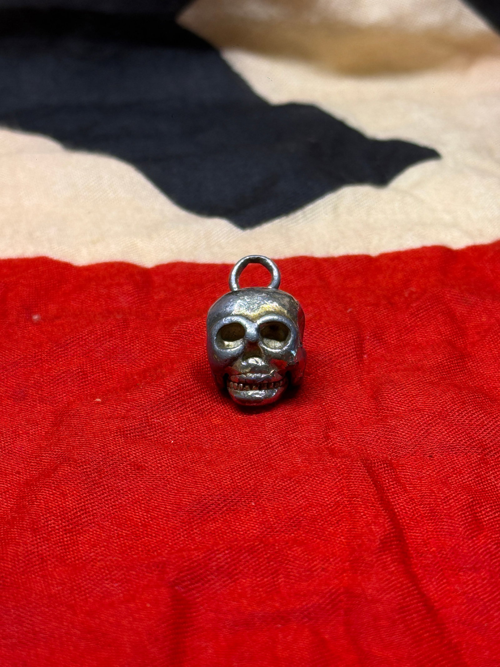 World War II German SS Totenkopf Skull Pendant Charm: Small cast-metal skull-form pendant displaying deeply recessed eye sockets, defined teeth, and an integral suspension loop for attachment to a chain, watch fob, or personal accessory. The reverse reve
