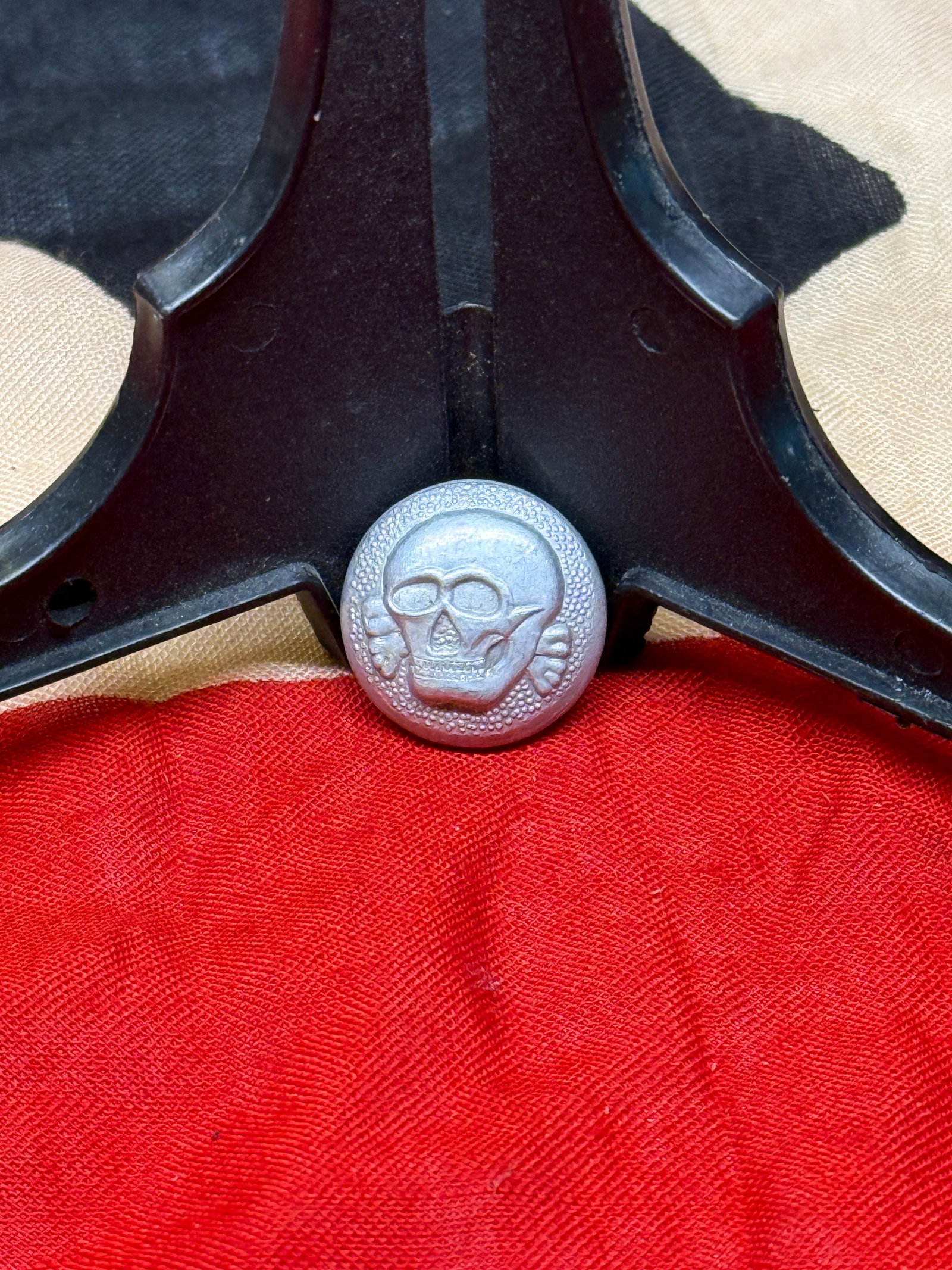 World War II German SS Totenkopf Uniform Button: Silver-gray metal uniform button bearing a raised Totenkopf (death’s head) motif consisting of a skull above crossed bones within a textured circular border. The reverse retains its original attachm