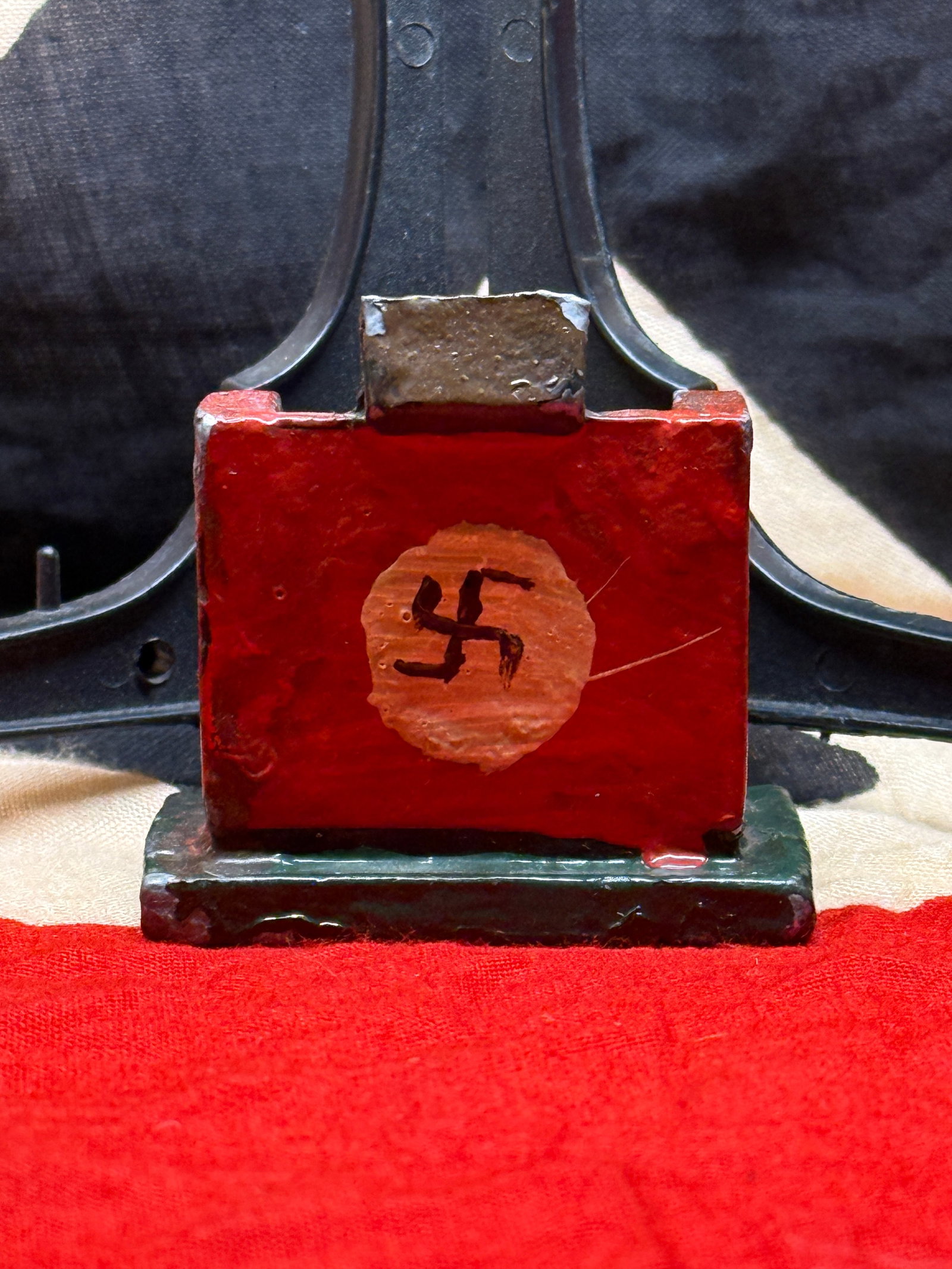 WW2 German Third Reich Political-Themed Miniature Desk Ornament: This small painted metal desk ornament features a red front panel bearing a black swastika within a circular field. The compact piece measures approximately 2½ inches in height and appears to h