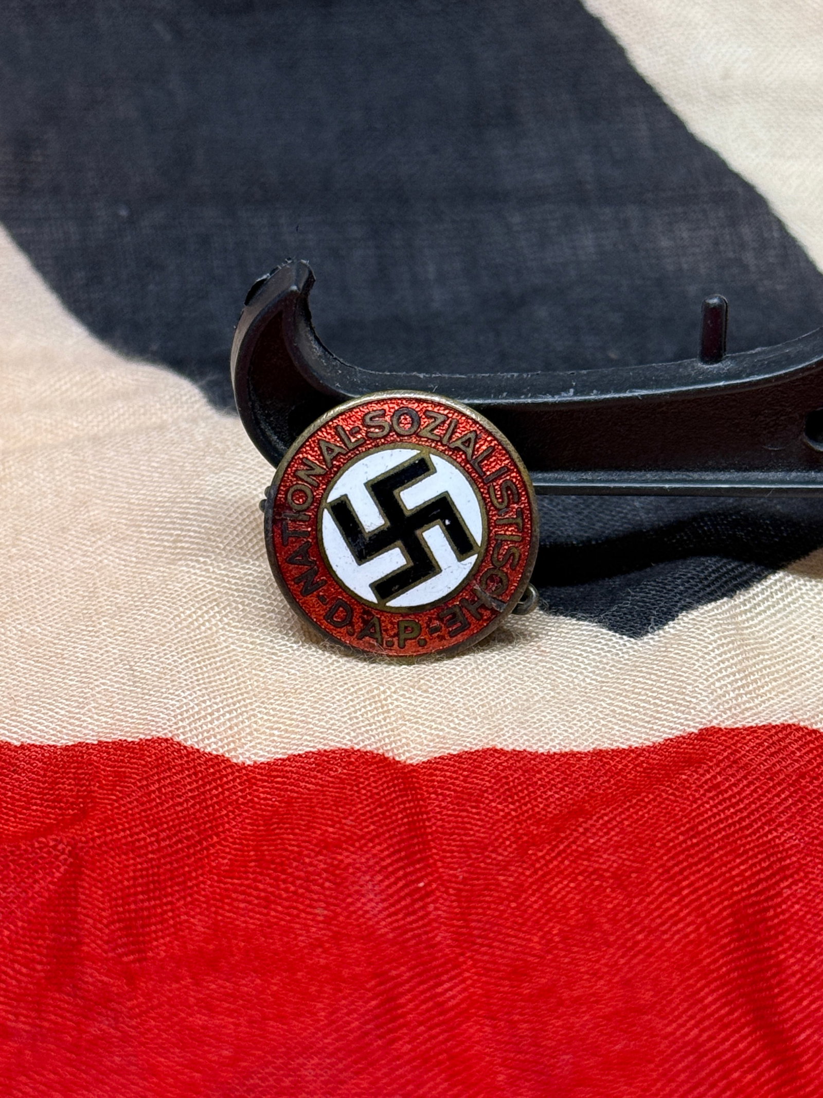 WWII German National Socialist German Workers’ Party (NSDAP) Membership Badge: This NSDAP membership badge bears the inscription “Nationalsozialistische D.A.P.” surrounding a black swastika set within a white enamel field and red circular border. The reverse retains a pe