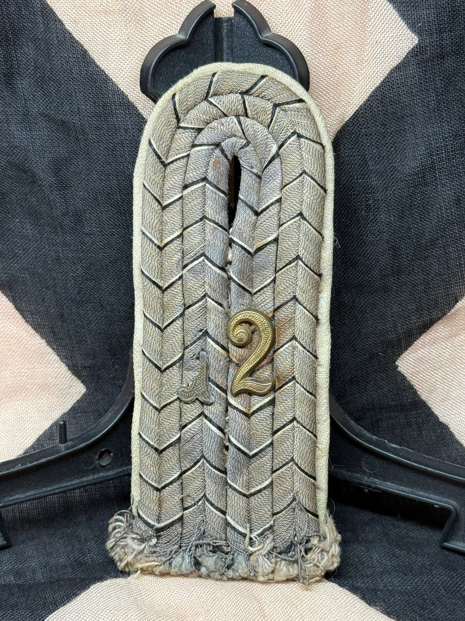 WWII German Army Shoulder Board with Regimental Numeral “2: Single Wehrmacht Army shoulder board featuring silver-gray woven chevron-pattern braid mounted on a feldgrau cloth base. Affixed to the face is a gilt metal numeral “2,” denoting affiliation w