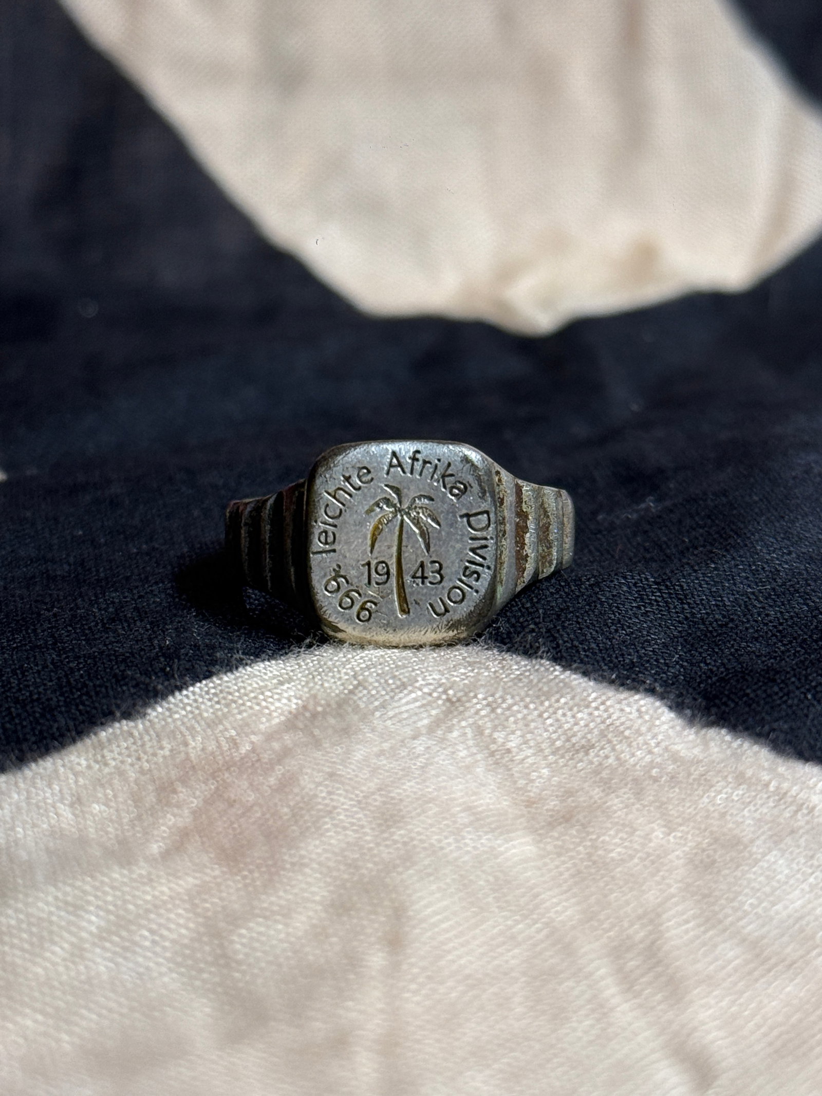 World War II German Leichte Afrika Division Commemorative Ring, Dated 1943: Cast metal commemorative ring featuring a palm tree motif at center surrounded by the inscription “Leichte Afrika Division” and the date “1943.” The ring’s bezel incorporates raised 