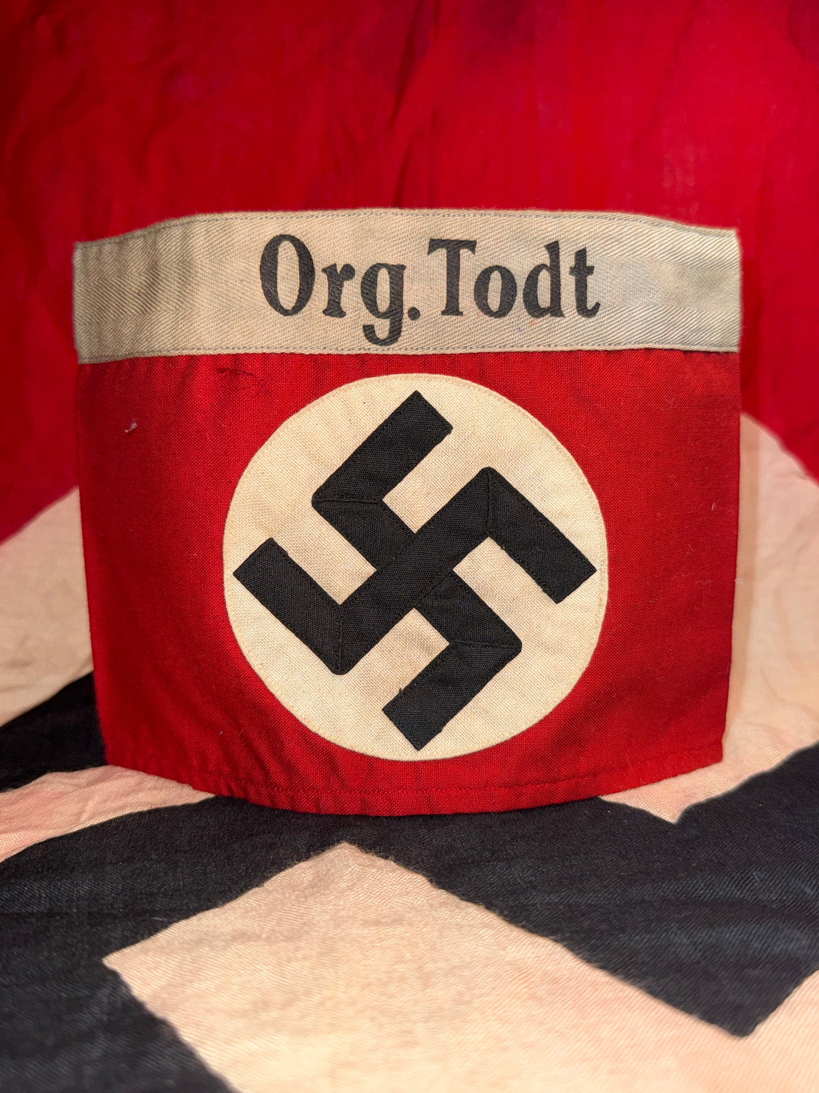 World War II German Organisation Todt (Org. Todt) Armband: Original red cloth armband bearing a black swastika applied to a white roundel and topped by a woven gray title band embroidered “Org. Todt” in black Gothic script. Organisation Todt (OT) was 