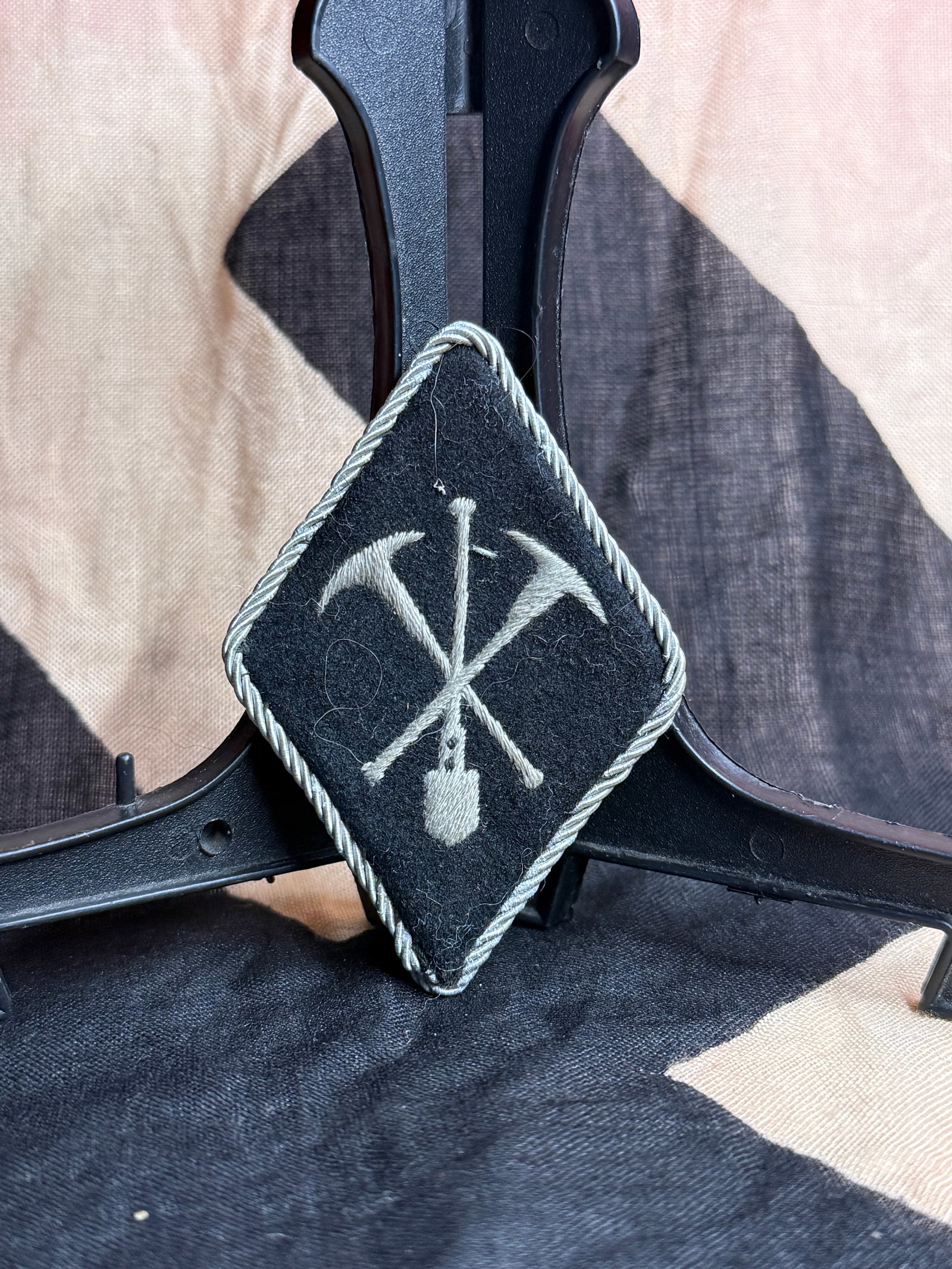 World War II German Waffen-SS Cavalry Sleeve Diamond Insignia: Black wool diamond-shaped sleeve insignia edged with silver-gray twisted cord piping and embroidered with crossed cavalry implements surrounding a central vertical lance motif. Sleeve diamonds of this